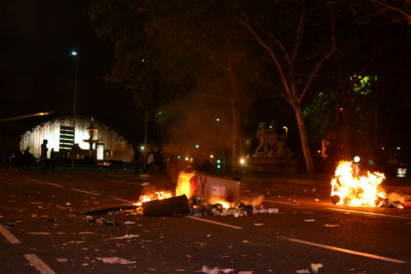 Varios contenedores y canecas de basura arden en medio de la calle. Al fondo, la estación de trenes de Atocha.