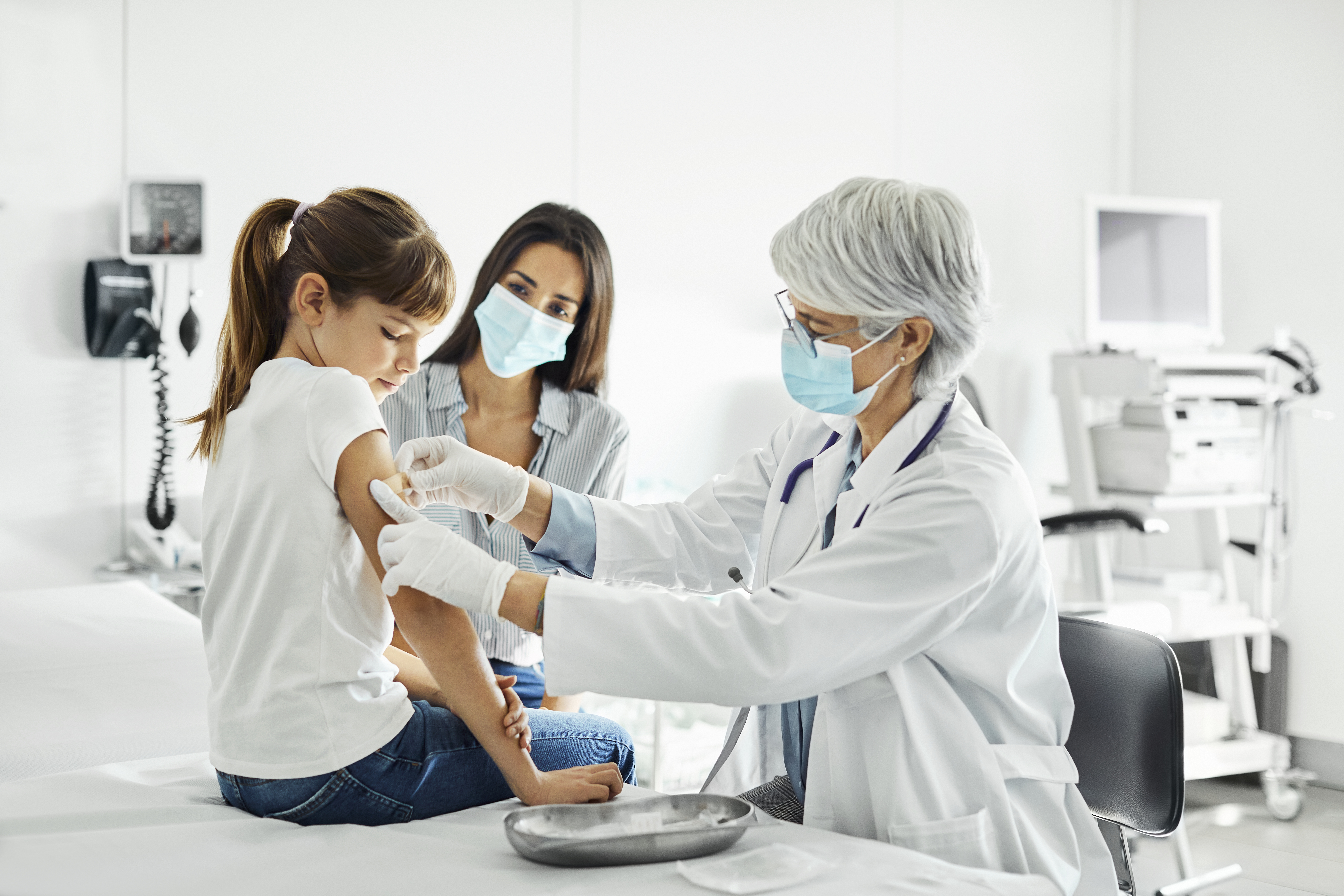 La pediatra está examinando al niño sentado en la mesa de examen. La familia está visitando la clínica durante el brote de COVID-19.