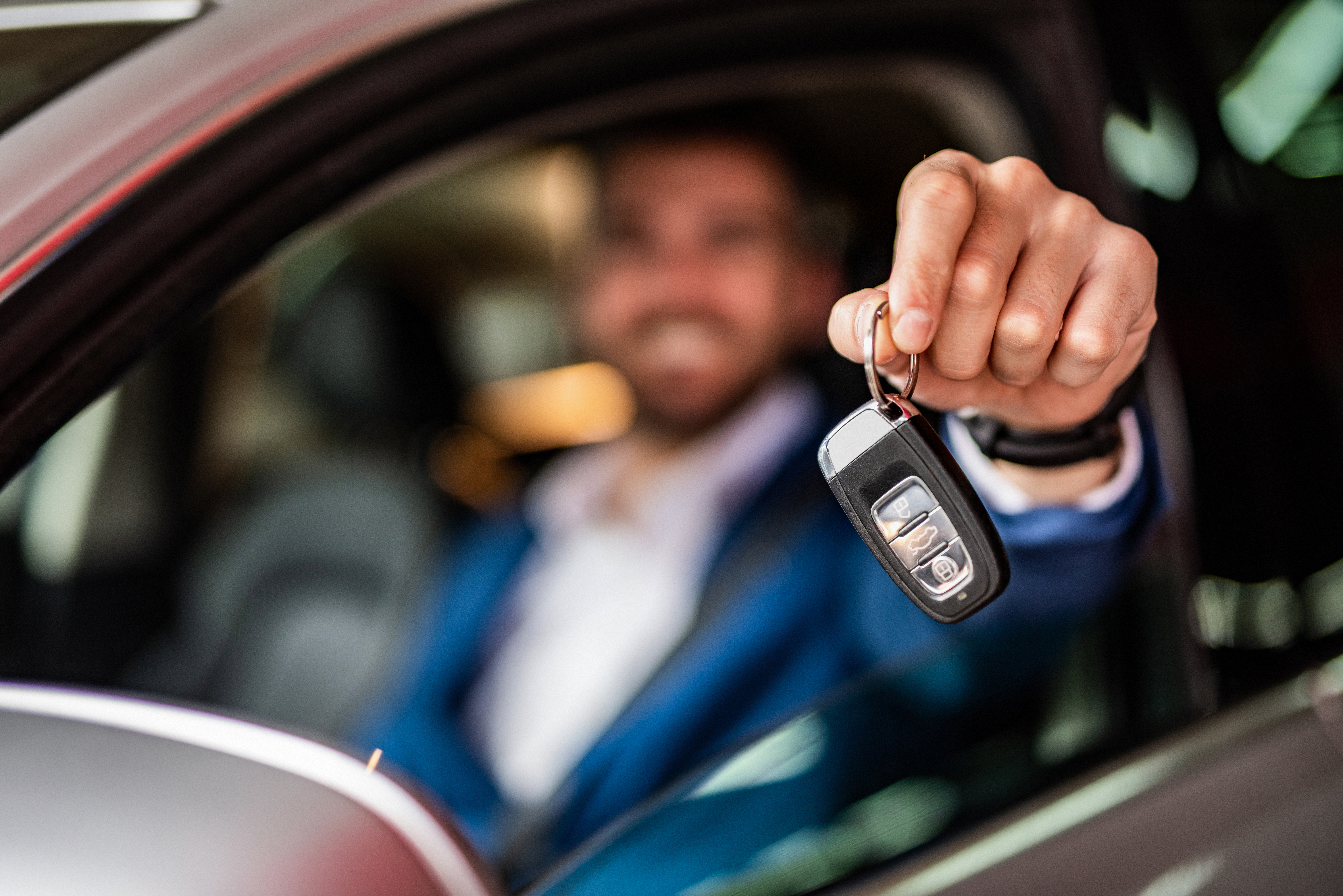 Photo of mid adult man sitting in new car and showing car keys. Focus on foreground.