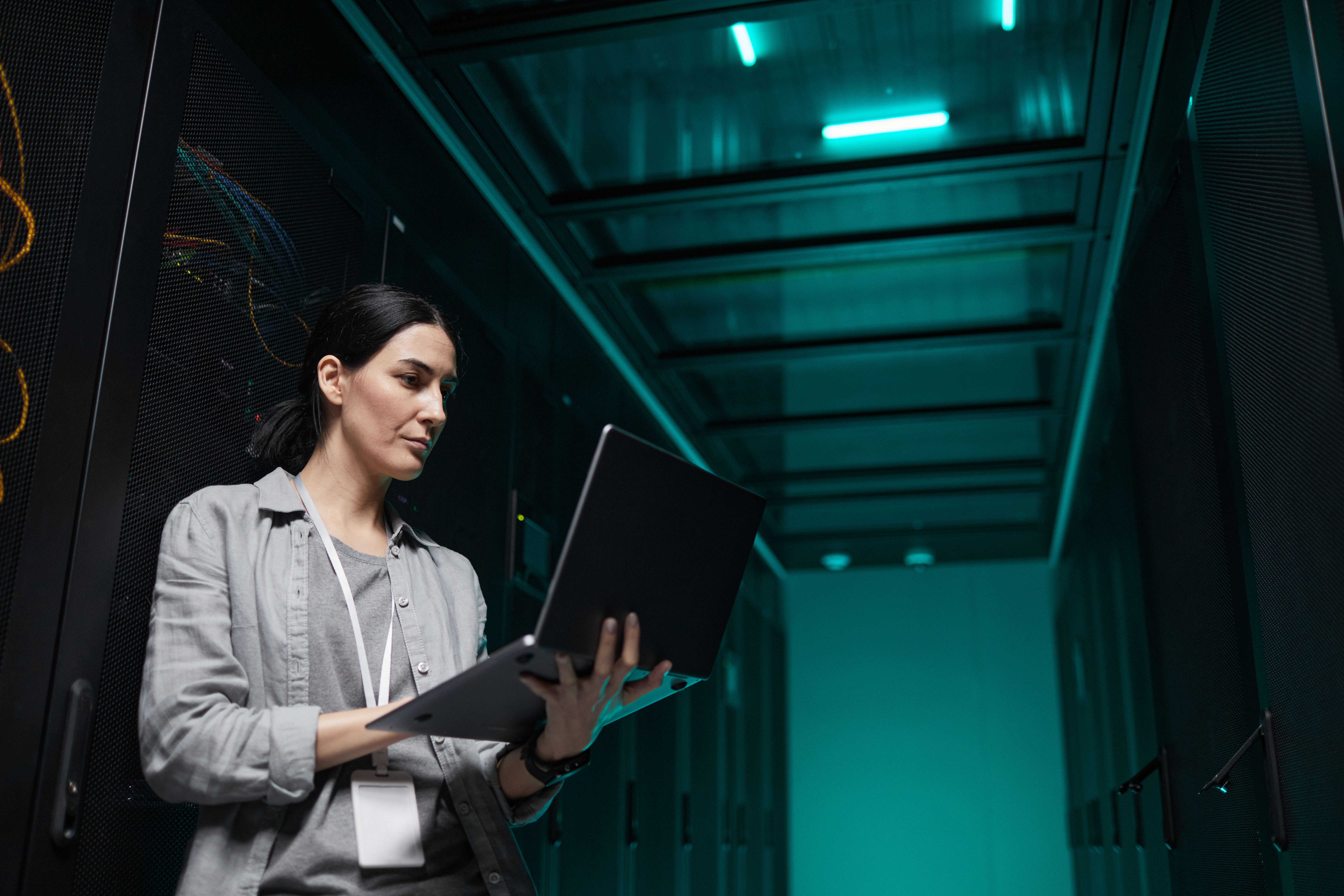 Retrato en la cintura de una ingeniera de datos sosteniendo una computadora portátil mientras trabaja con una supercomputadora en la sala de servidores, copiando espacio