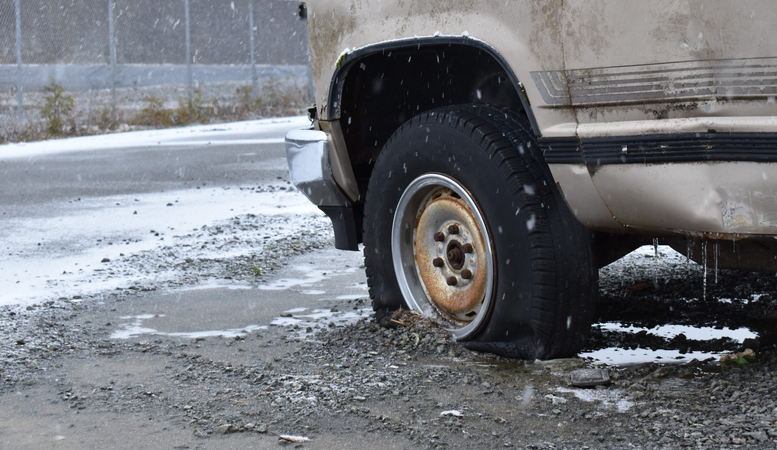 Flat tire on an old rusty truck.   Bad weather, snow falling.