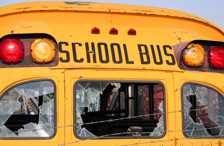 A close-up of the rear of an old school bus with broken windows and rusting paint.