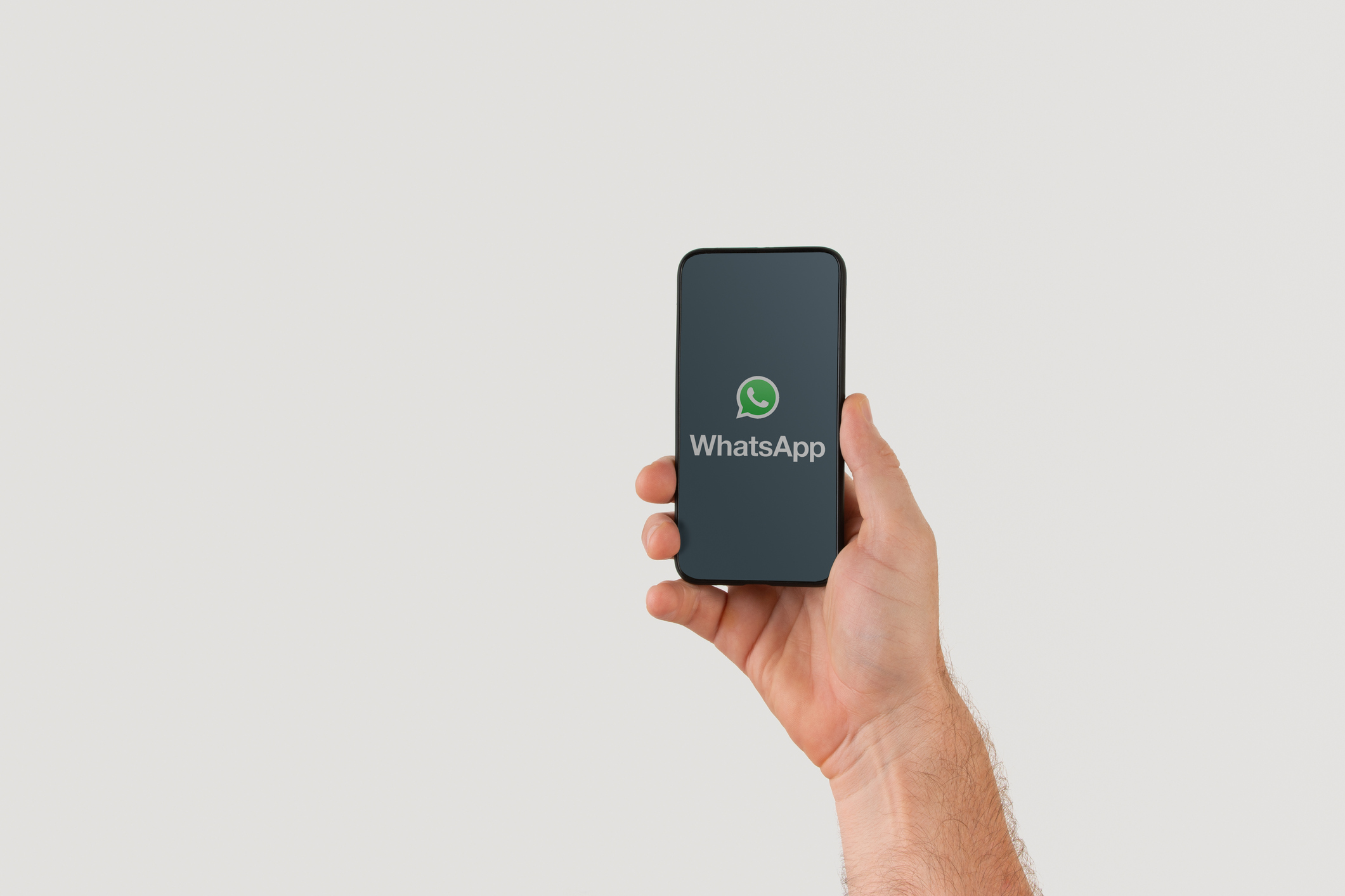 Hand holding smart phone with popular online text / call application "WhatsApp" logo on screen. Illustrative editorial image with copy space for text.