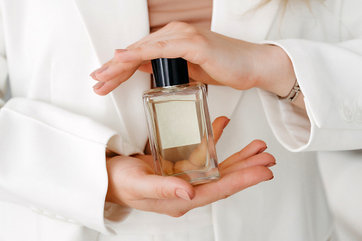 Hands of a beautiful young woman with a bottle of floral perfume on a light background