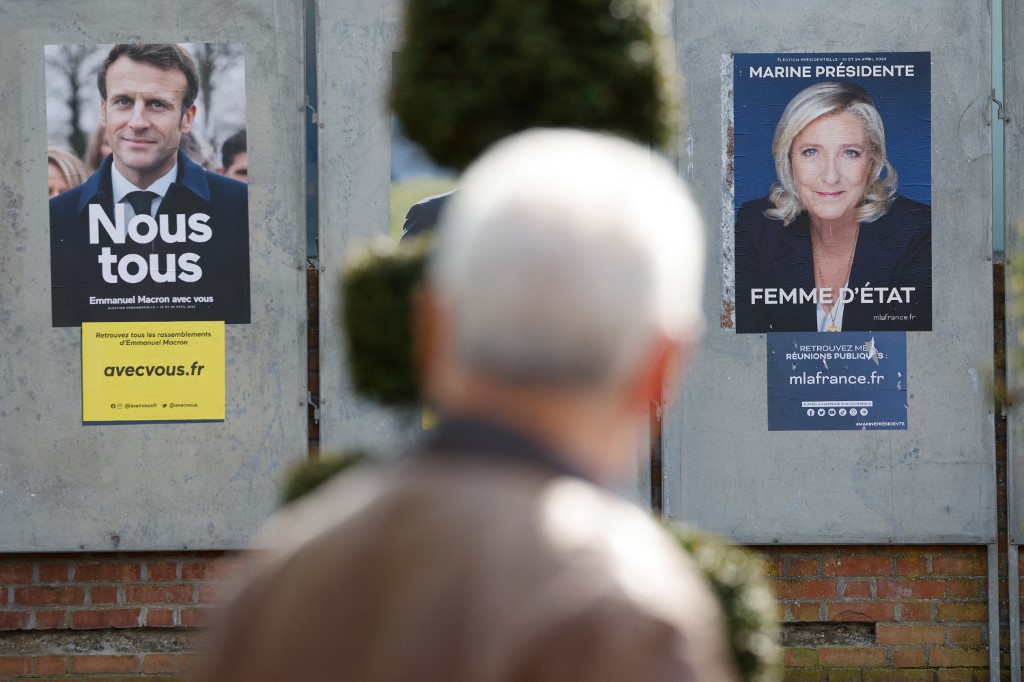Un hombre camina junto a carteles de campaña de los candidatos presidenciales franceses, el actual presidente Emmanuel Macron (L) y la candidata presidencial del partido de extrema derecha francés Rassemblement National (RN) Marine Le Pen en Denain, el 11 de abril de 2022. Emmanuel Macron obtuvo el 27,85 por ciento de los votos. en la primera ronda de las elecciones presidenciales de Francia, mientras que la veterana de extrema derecha Marine Le Pen obtuvo un 23,15 por ciento, según los resultados finales del Ministerio del Interior el lunes.(Foto por Ludovic MARIN / AFP)