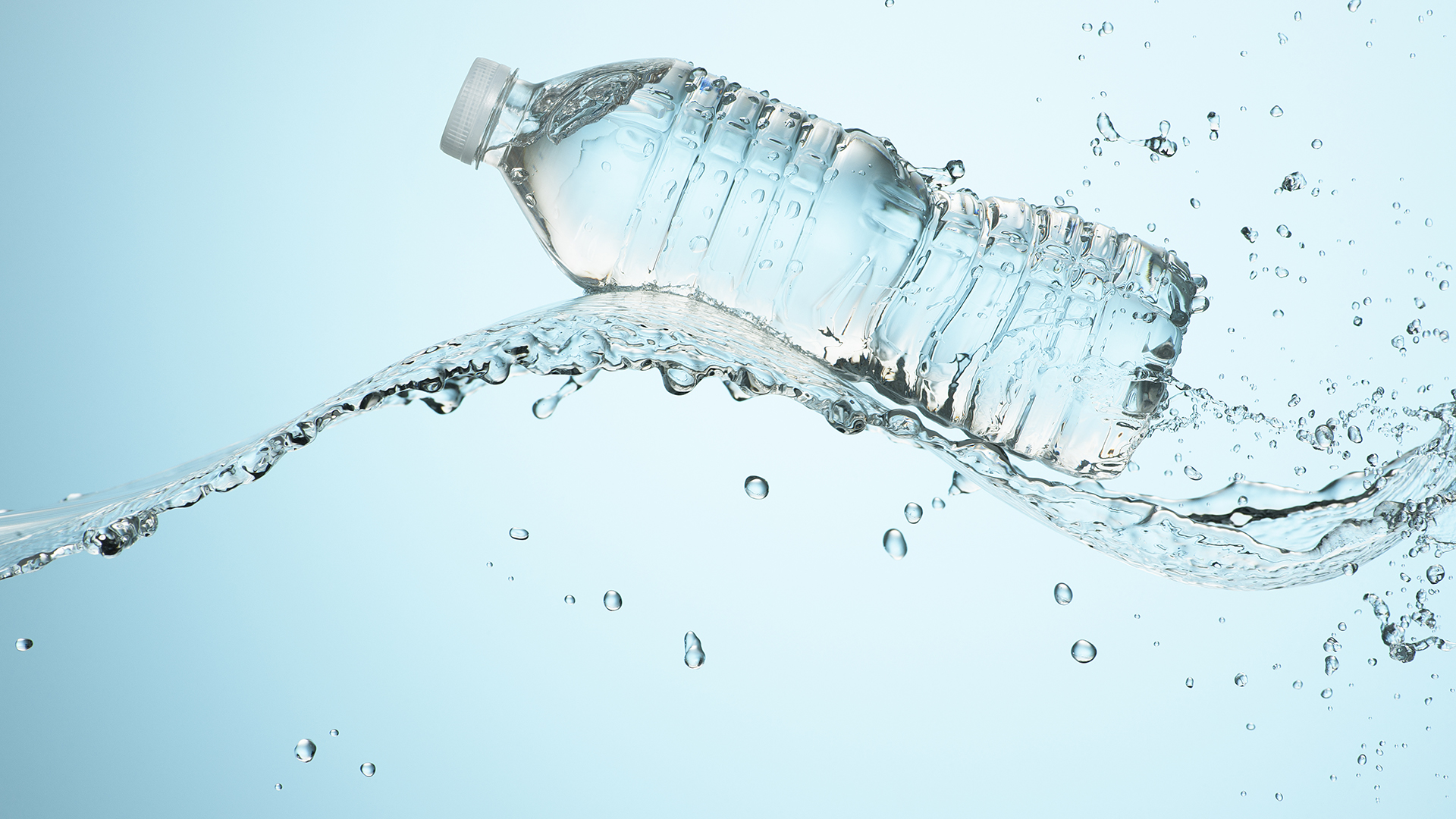 Gran salpicadura de agua limpia y refrescante con una botella de agua saludable en el estudio sobre un fondo azul claro para una vida saludable