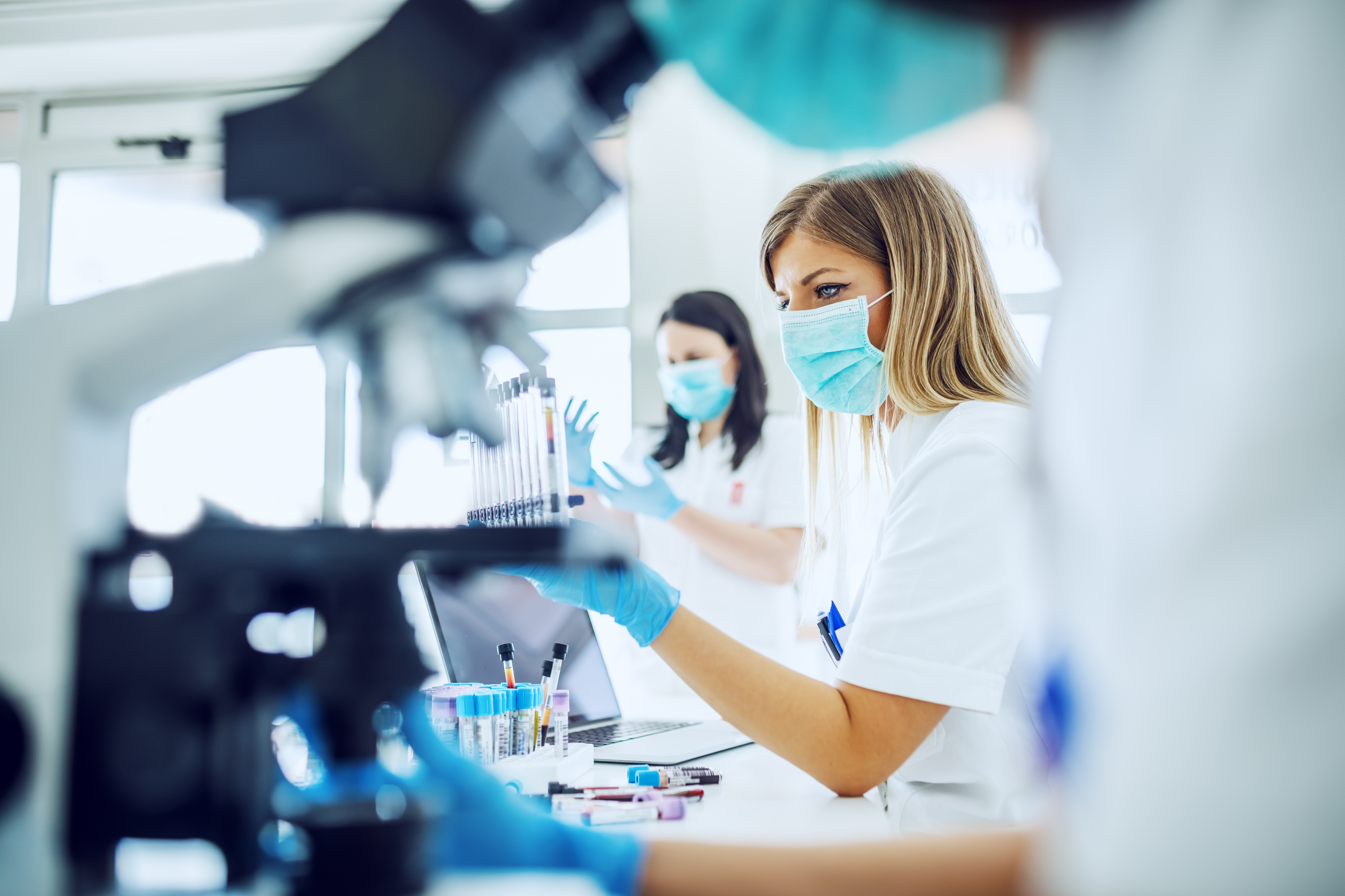 Small group of female laboratory assistants checking blood, using microscope and doing test for bacteria.