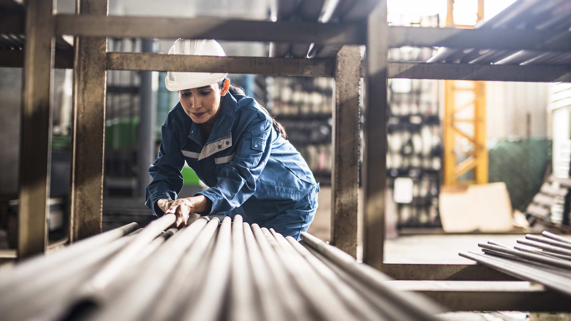 Trabajadora de una fábrica de acero en el trabajo moviendo postes de acero