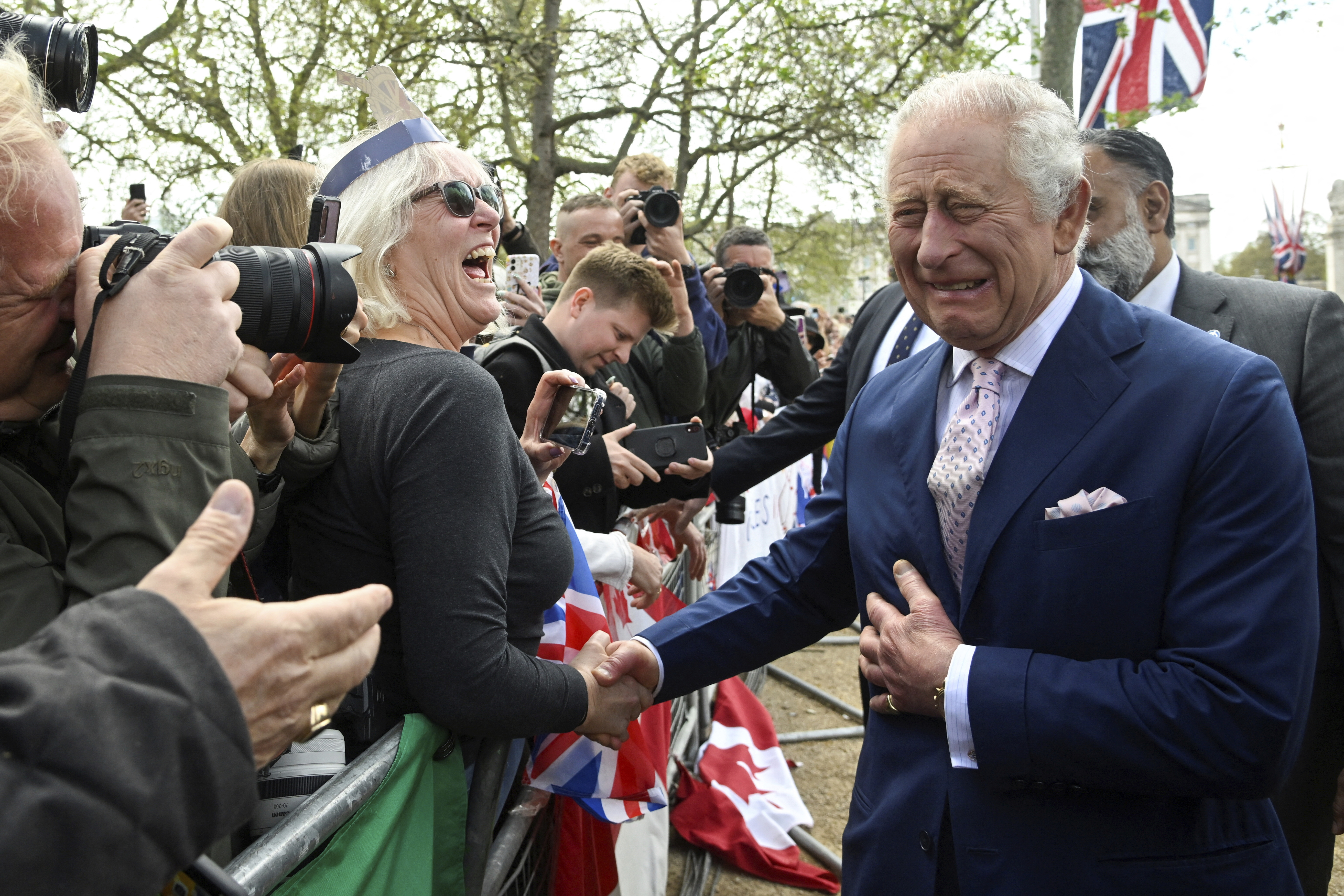 FILE  - Britain's King Charles III greets well-wishers outside Buckingham Palace, in London, Friday, May 5, 2023 a day before his coronation takes place at Westminster Abbey. A year after the death of Queen Elizabeth II triggered questions about the future of the British monarchy, King Charles III’s reign has been marked more by continuity than transformation, by changes in style rather than substance.  (Toby Melville, Pool via AP, File)