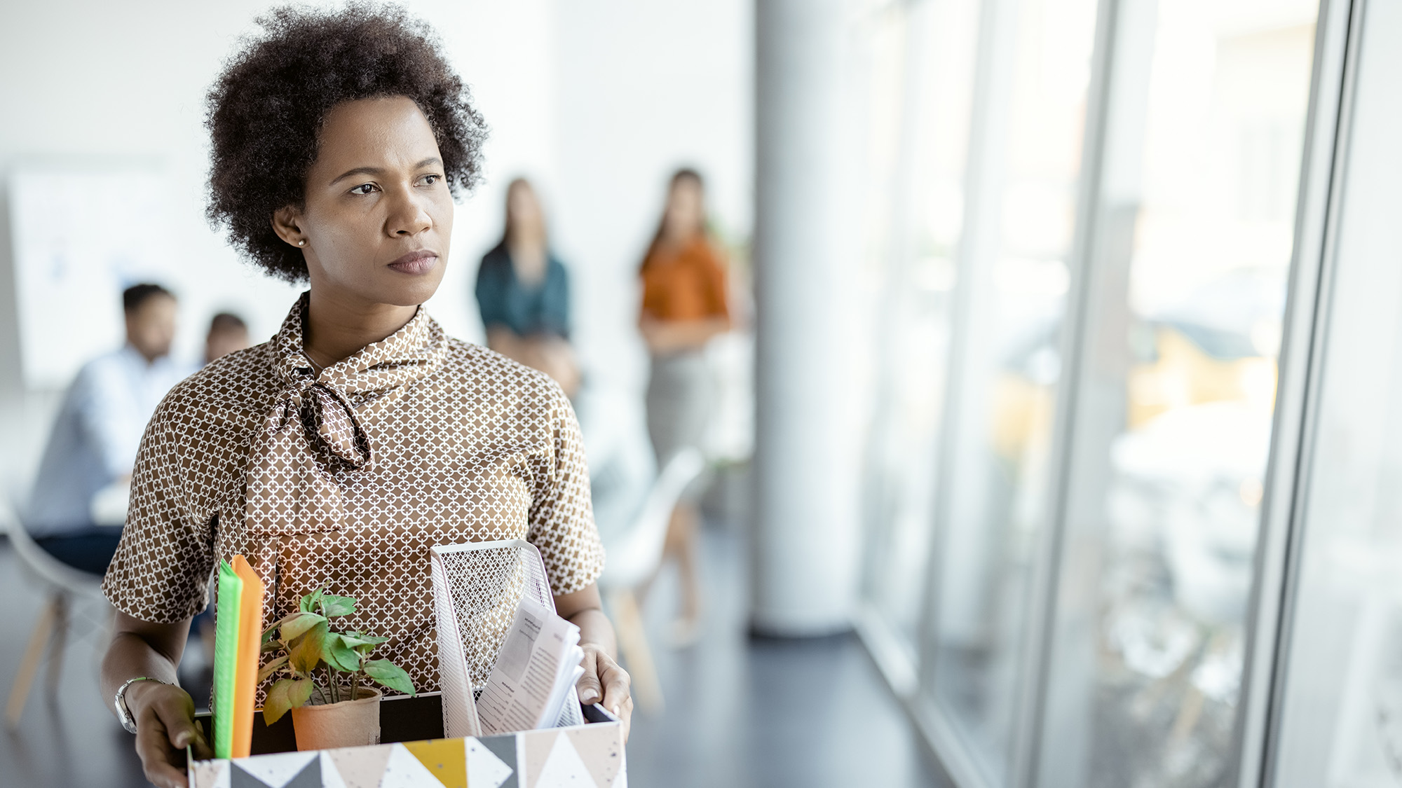 Mujer africana madura siendo despedida del trabajo. La mujer camina por la oficina, cargando una caja con objetos personales. Concepto de negocio, despido y pérdida de empleo