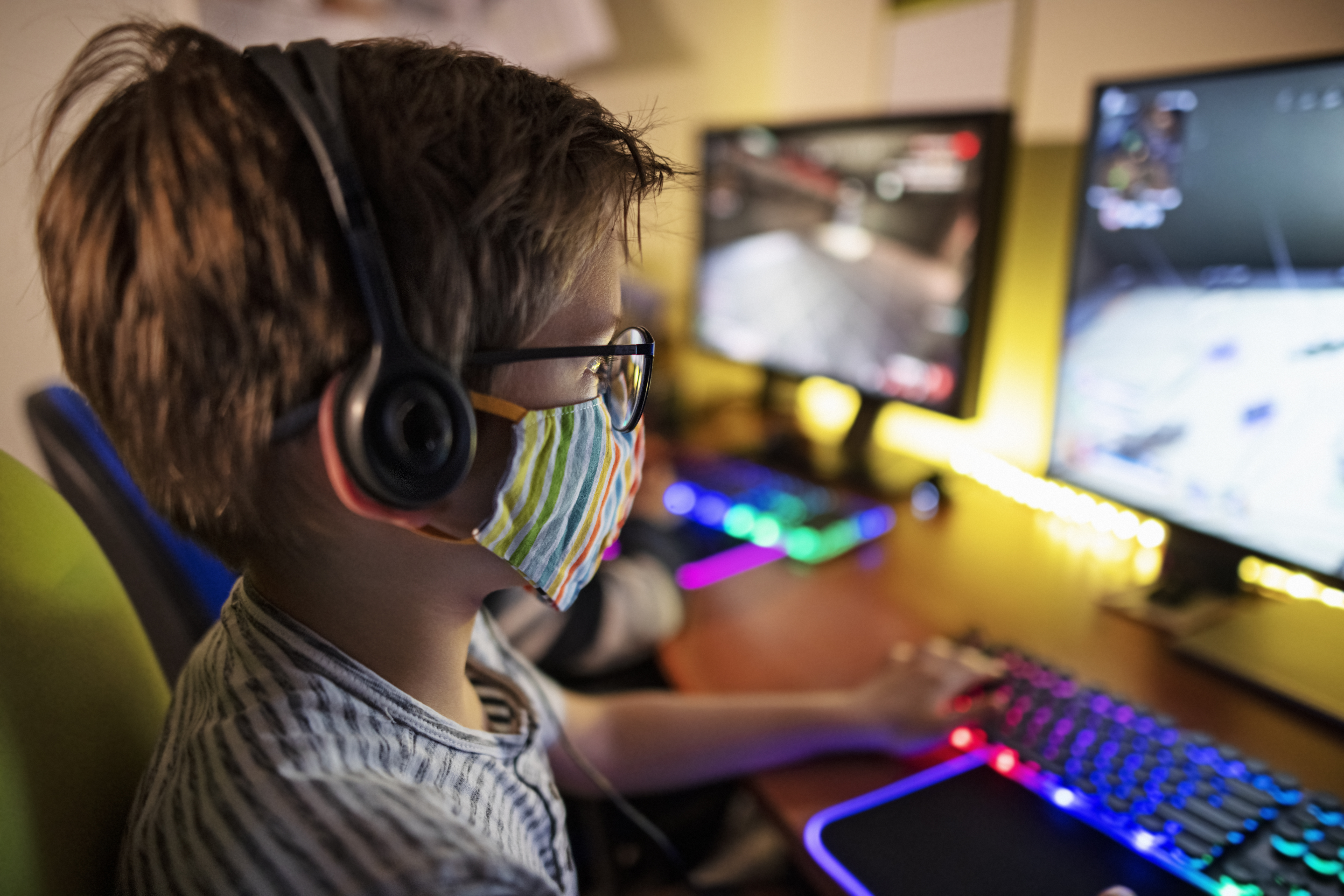 Durante la pandemia de COVID-19, los niños juegan videojuegos multijugador en equipo usando una computadora de escritorio. Los niños llevan una mascarilla quirúrgica para evitar la propagación del coronavirus a toda la familia.Nikon D850