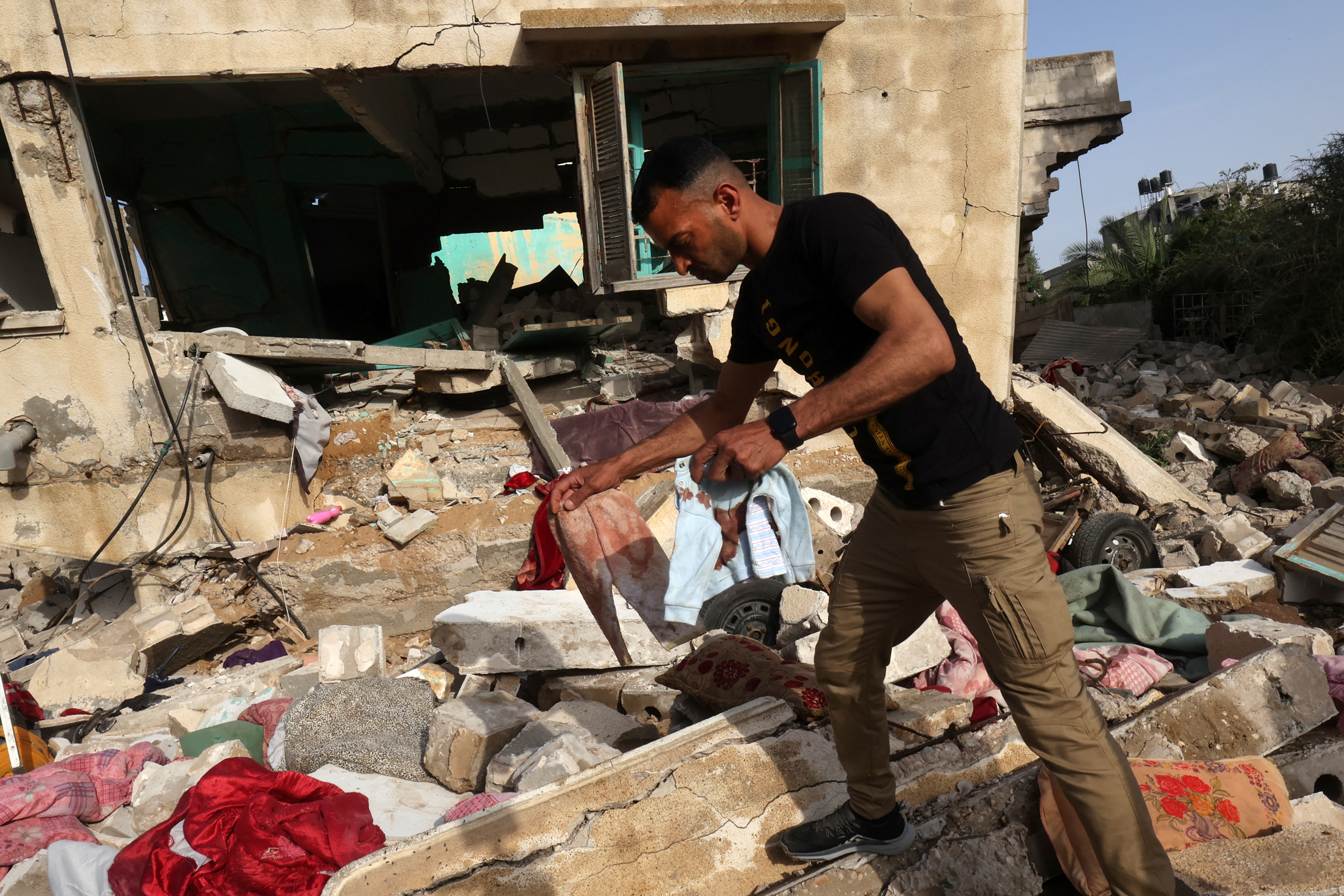 A man retrieves blood-stained baby clothes on May 11, 2023, from the rubble of the house of Ahmed Abu-Deka, the deputy of the commander of a rocket launch unit killed by Israel on May 10. Islamic Jihad confirmed it has lost five military leaders in strikes in recent days, including Abu-Deka. (Photo by SAID KHATIB / AFP)