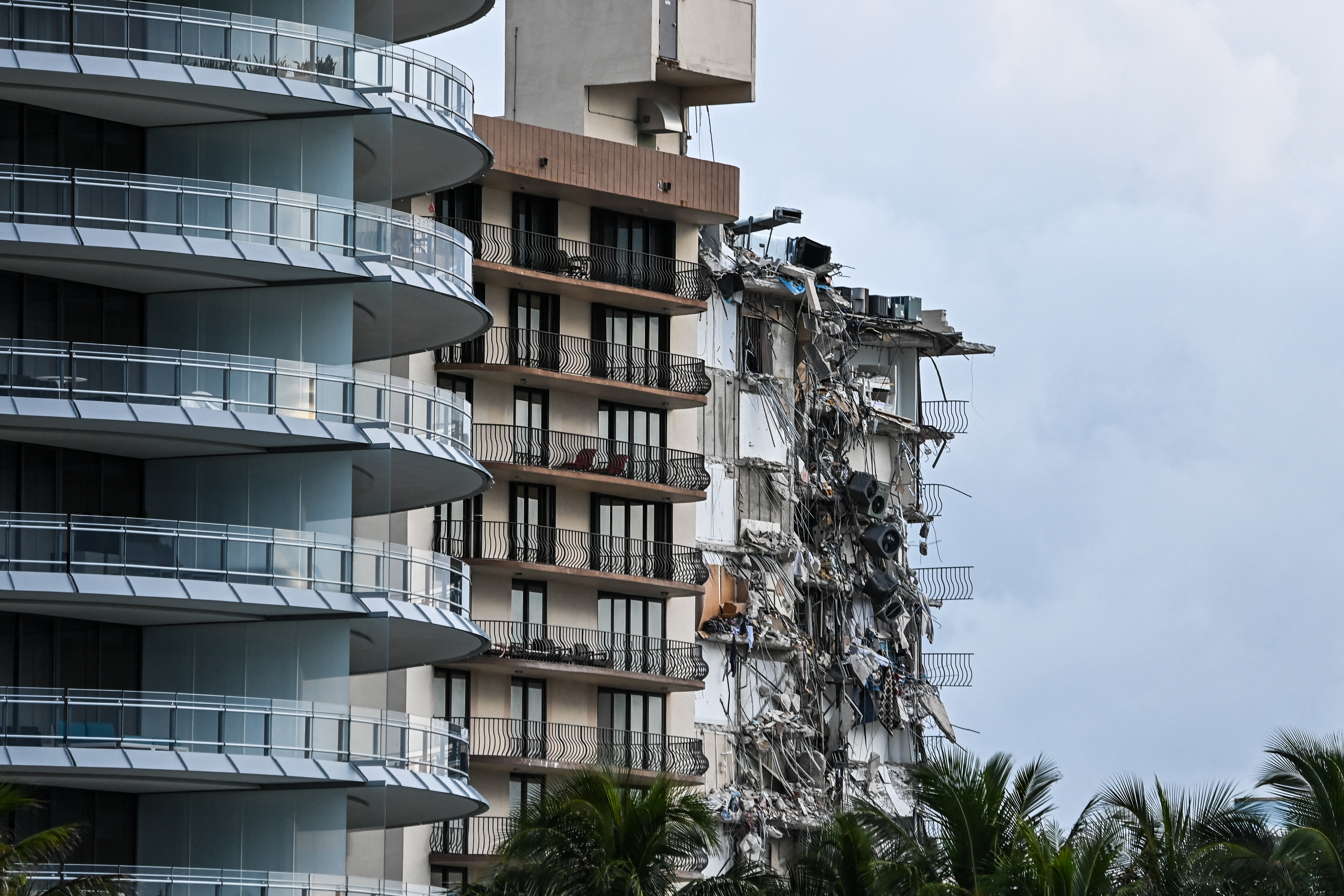 Rubble hangs from a partially collapsed building in Surfside north of Miami Beach, on June 24, 2021. - The multi-story apartment block in Florida partially collapsed early June 24, sparking a major emergency response. Surfside Mayor Charles Burkett told NBC�s Today show: �My police chief has told me that we transported two people to the hospital this morning at least and one has died. We treated ten people on the site.� (Photo by CHANDAN KHANNA / AFP)