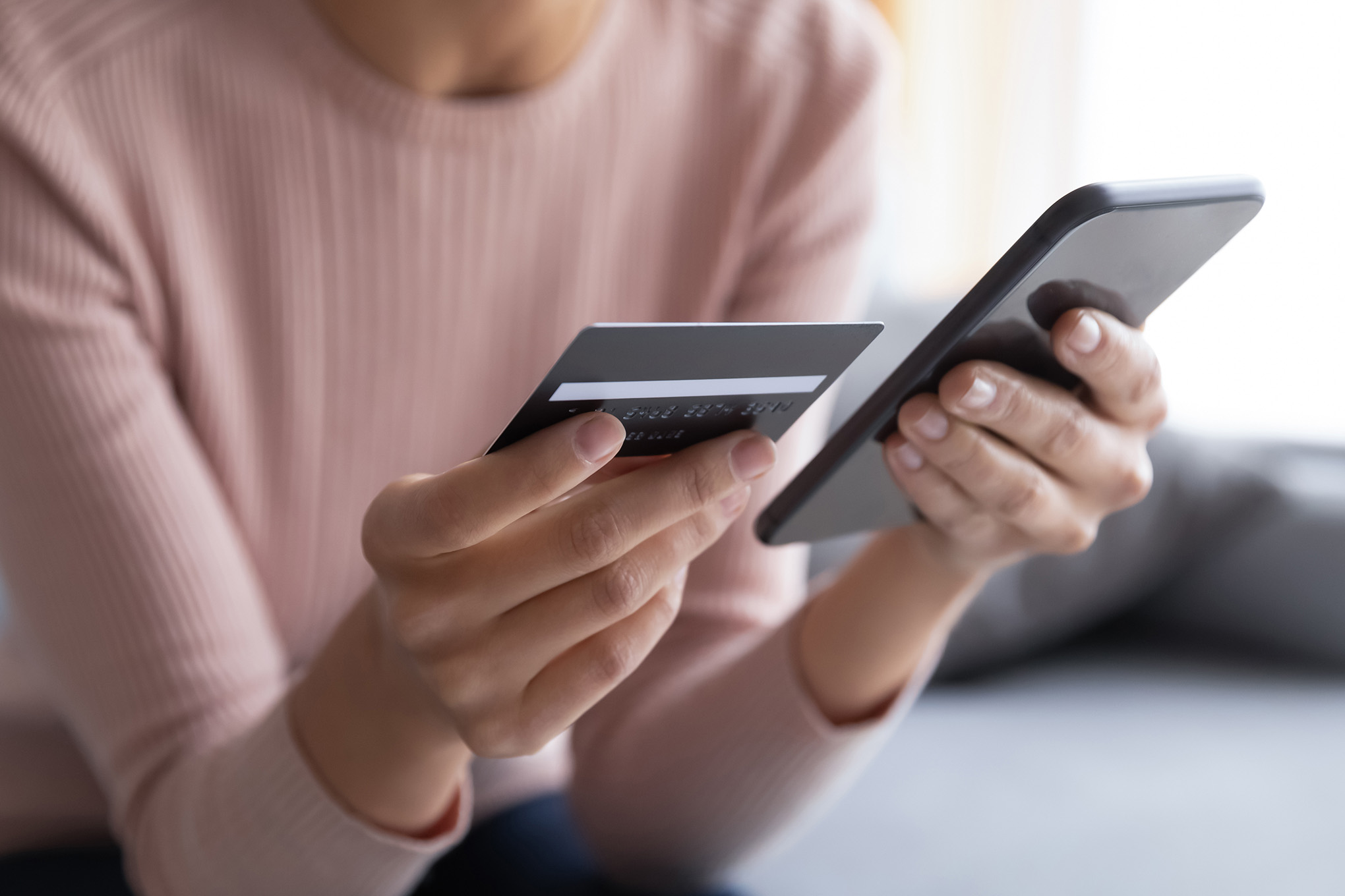 Close up female hands holding credit card and smartphone, young woman paying online, using banking service, entering information, shopping, ordering in internet store, doing secure payment