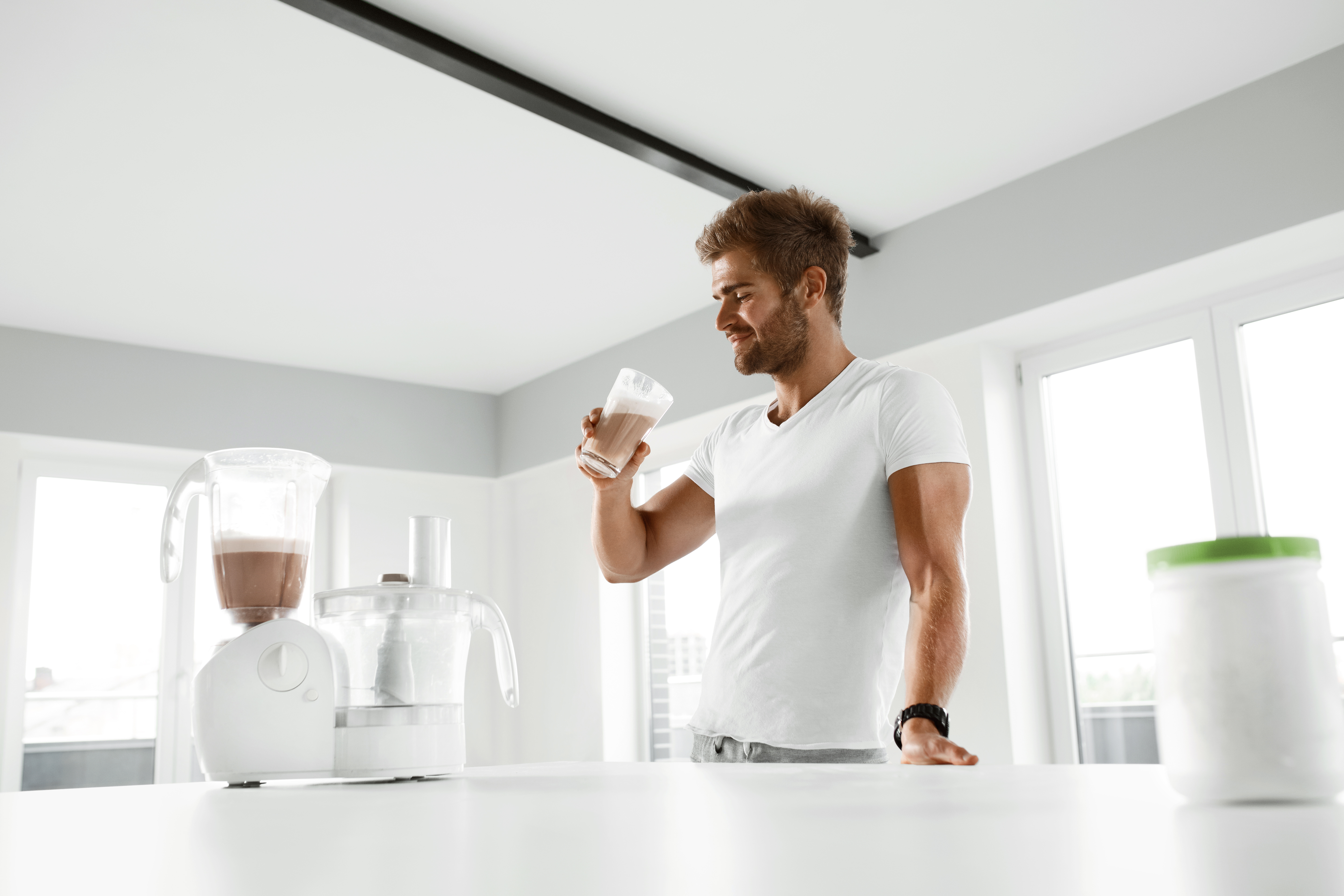 Nutrition Supplements. Handsome Happy Smiling Man With Muscular Body Drinking Protein Shake Before Workout. Sexy Athletic Fitness Male Model Enjoying Sports Drink Indoors. Bodybuilding, Healthy Eating