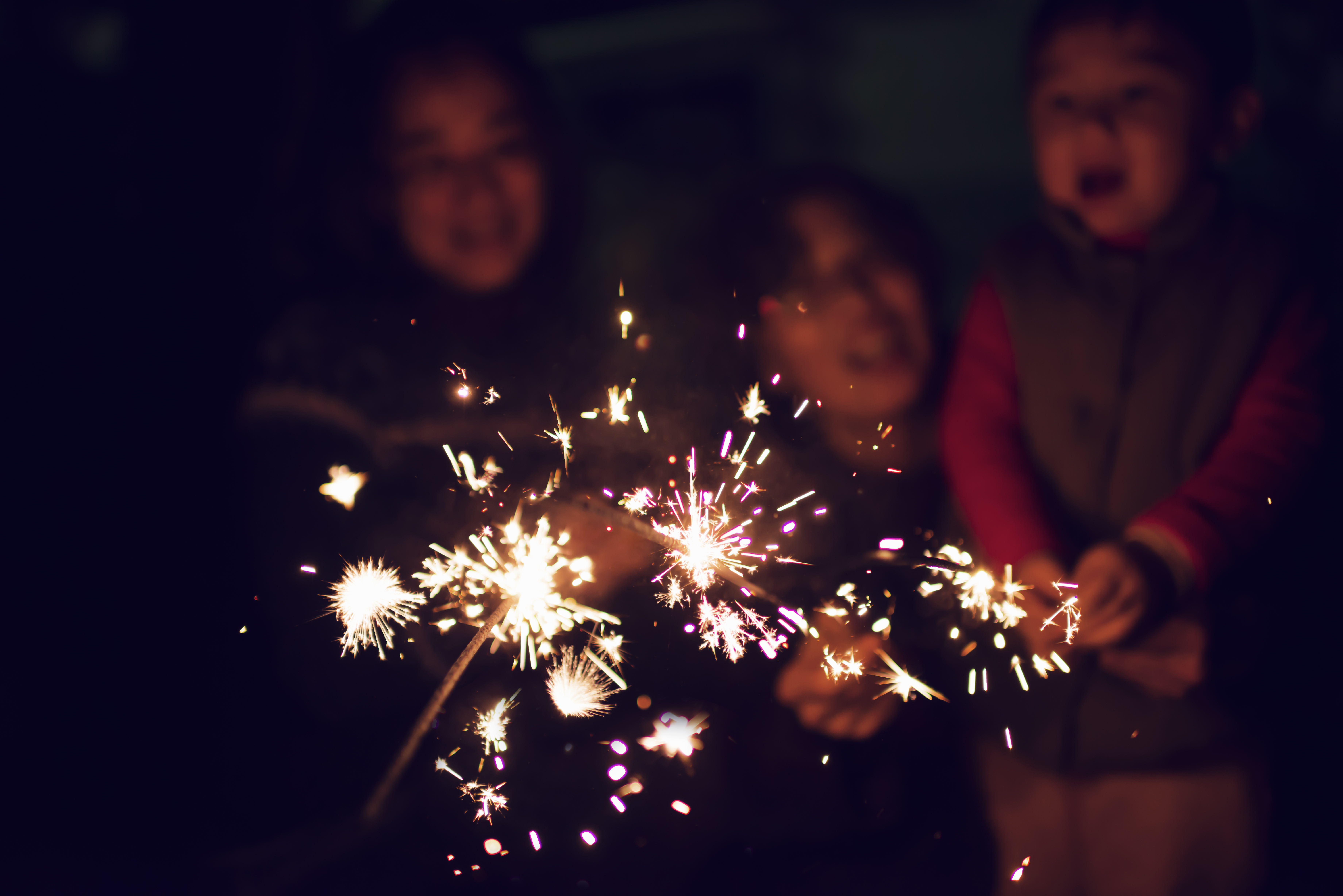 A child is playing sparklers with his family at night