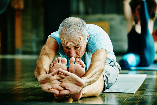 Mature man in seated forward bend pose during yoga class in studio