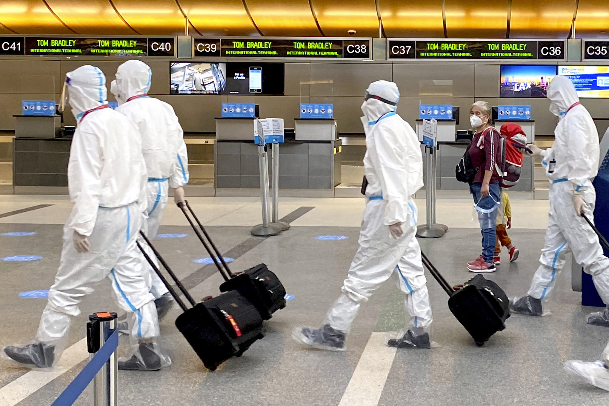 Una mujer, acompañada de un niño, mira cómo una tripulación de la aerolínea que lleva todo el equipo de protección personal contra COVID-19 camina a través de la terminal internacional en el Aeropuerto Internacional de Los Ángeles, el martes 17 de noviembre de 2020. Foto: Keith Birmingham / The Orange County Register vía AP