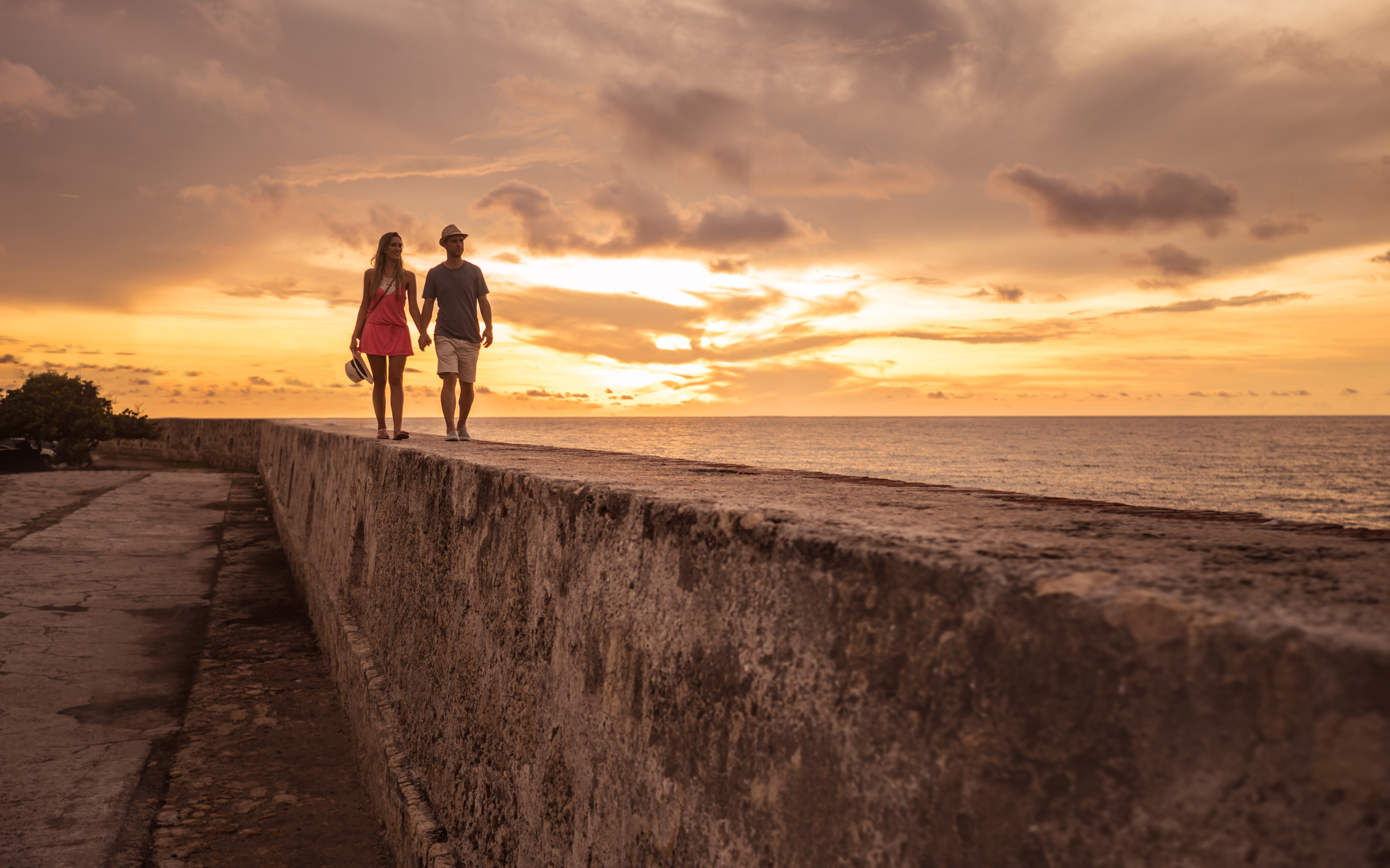 Turistas disfrutando de la hermosa puesta de sol mientras caminan sobre la pared en Cartagena - gente viajando
