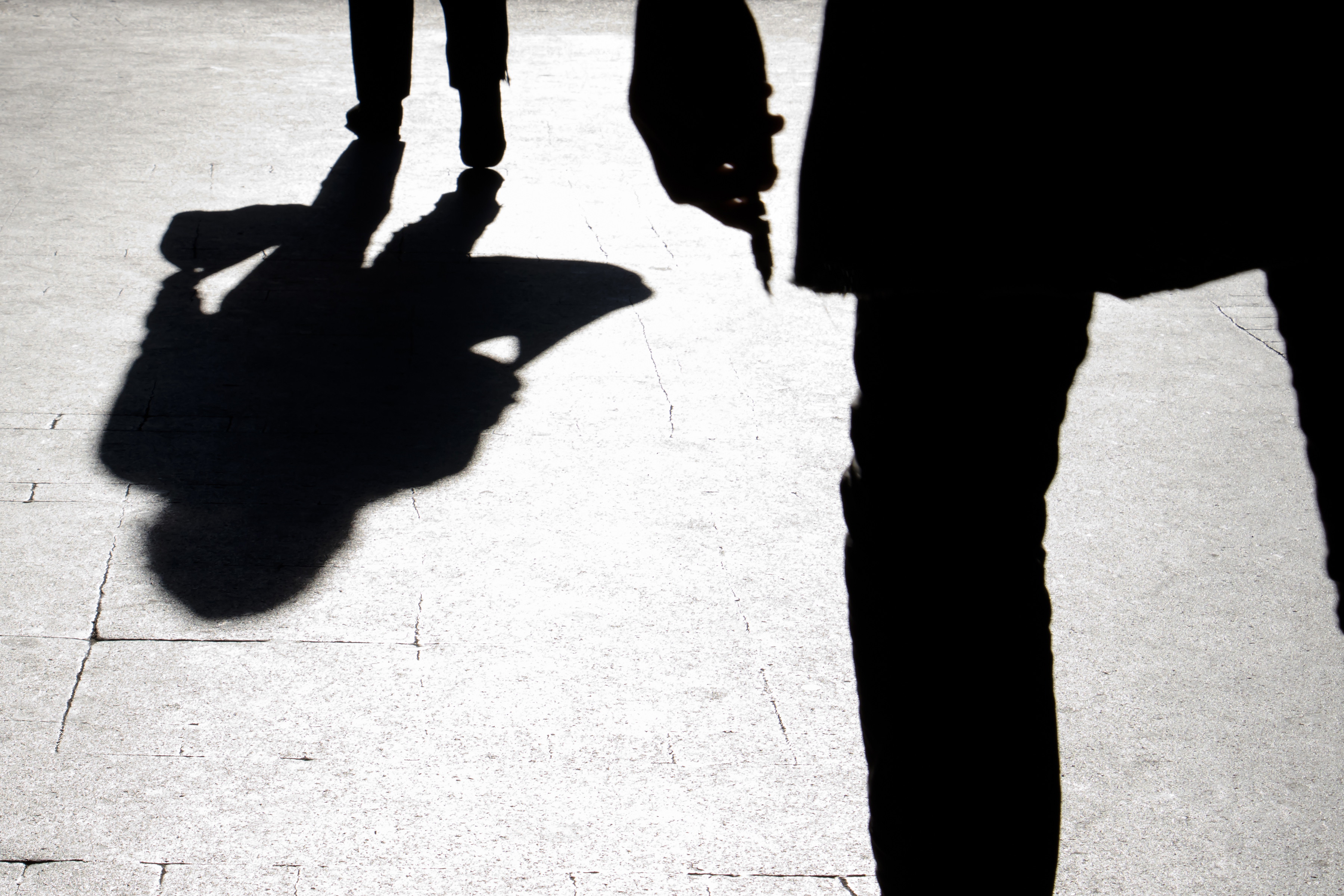 Blurry silhouette and shadow of a woman carrying a bag and a man holding sharp object following her, in the city street in the night