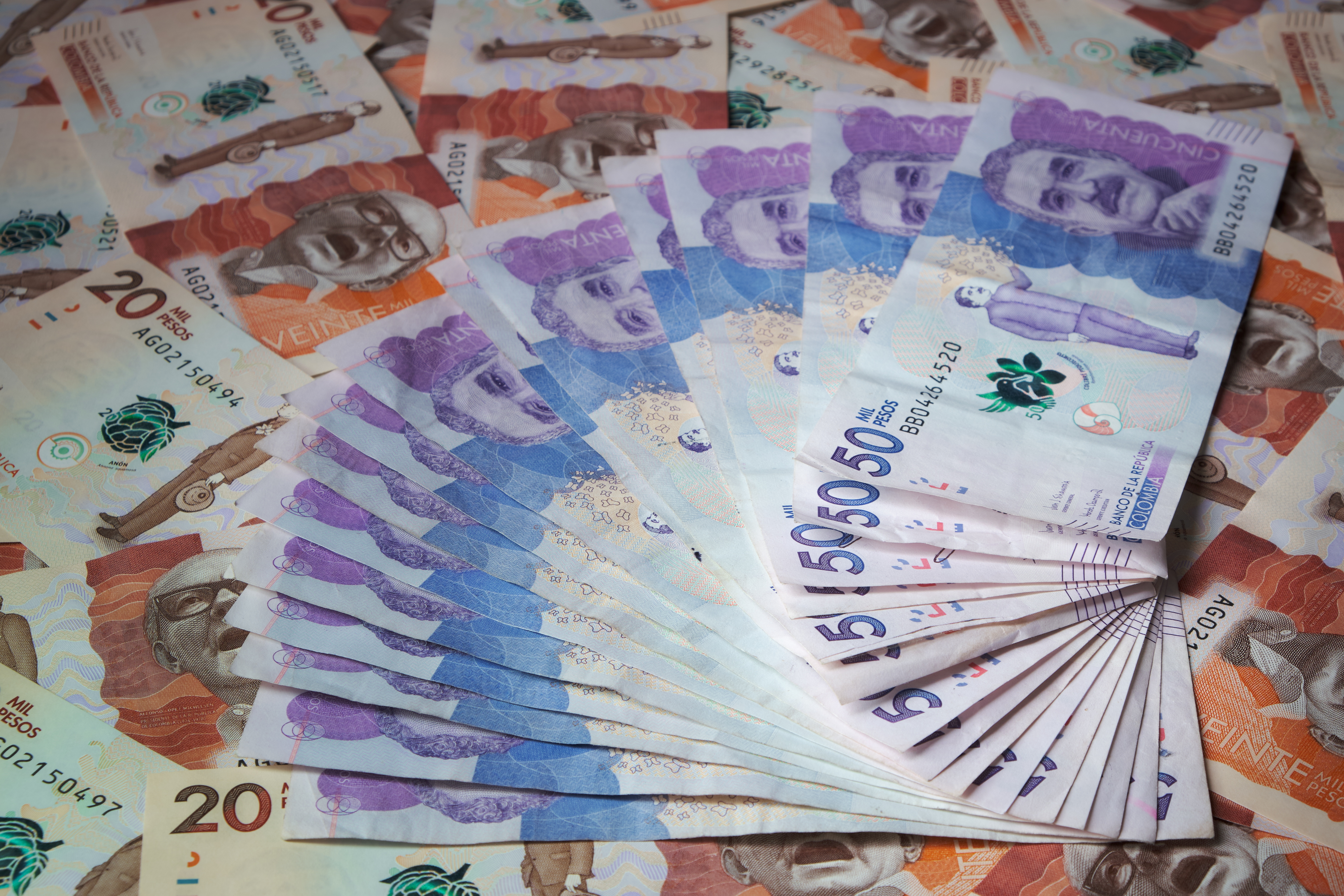 Billetes de 50000 pesos colombianos en forma de abanico sobre un fondo de billetes de 20000 pesos