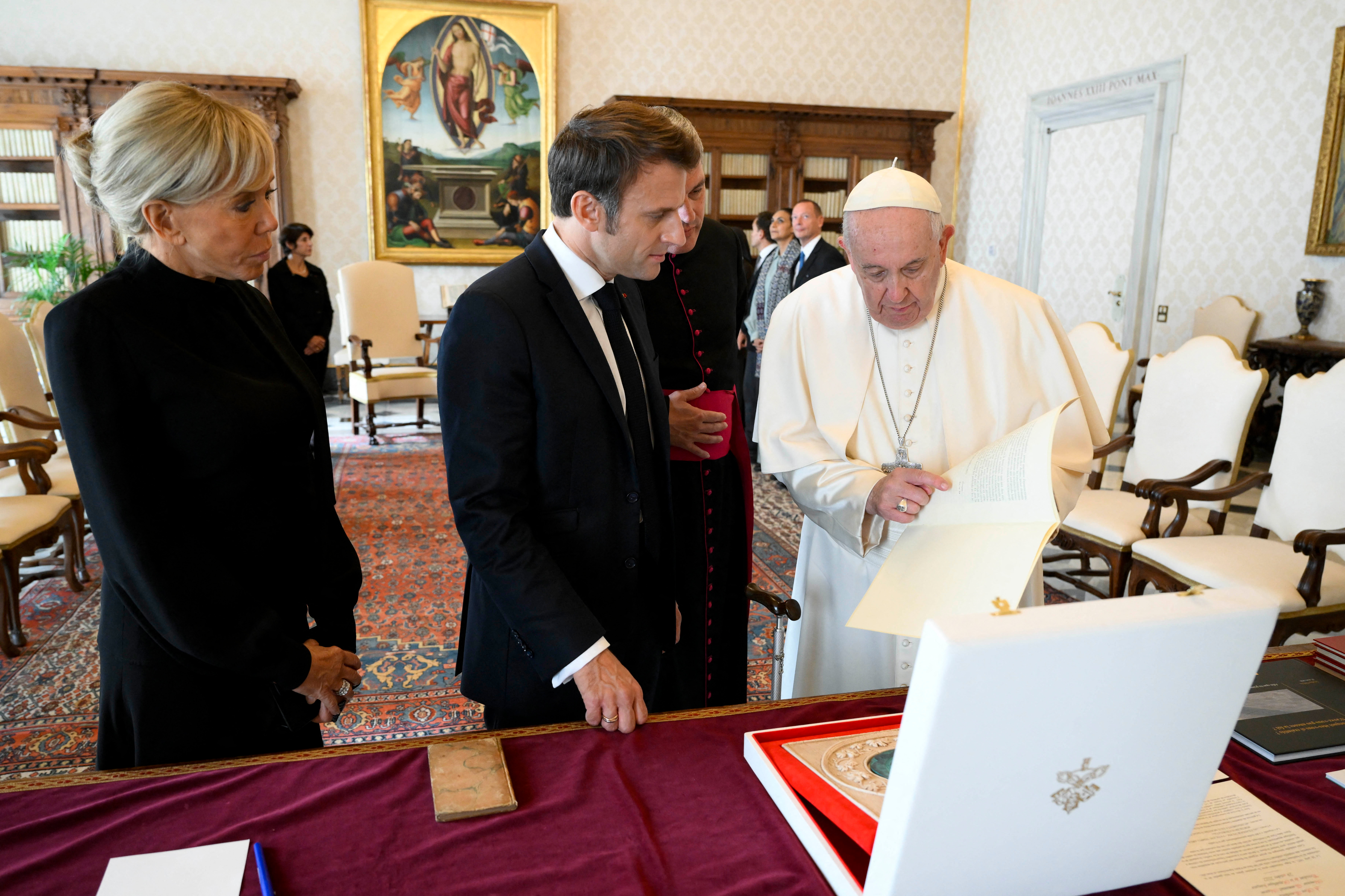 Esta foto de mano tomada y publicada el 24 de octubre de 2022 por la oficina de prensa del Vaticano, Vatican Media, muestra al papa Francisco (R) intercambiando regalos con el presidente francés Emmanuel Macron (C) y su esposa Brigitte Macron (L) durante una audiencia privada en el Vaticano. (Photo by VATICAN MEDIA / AFP)