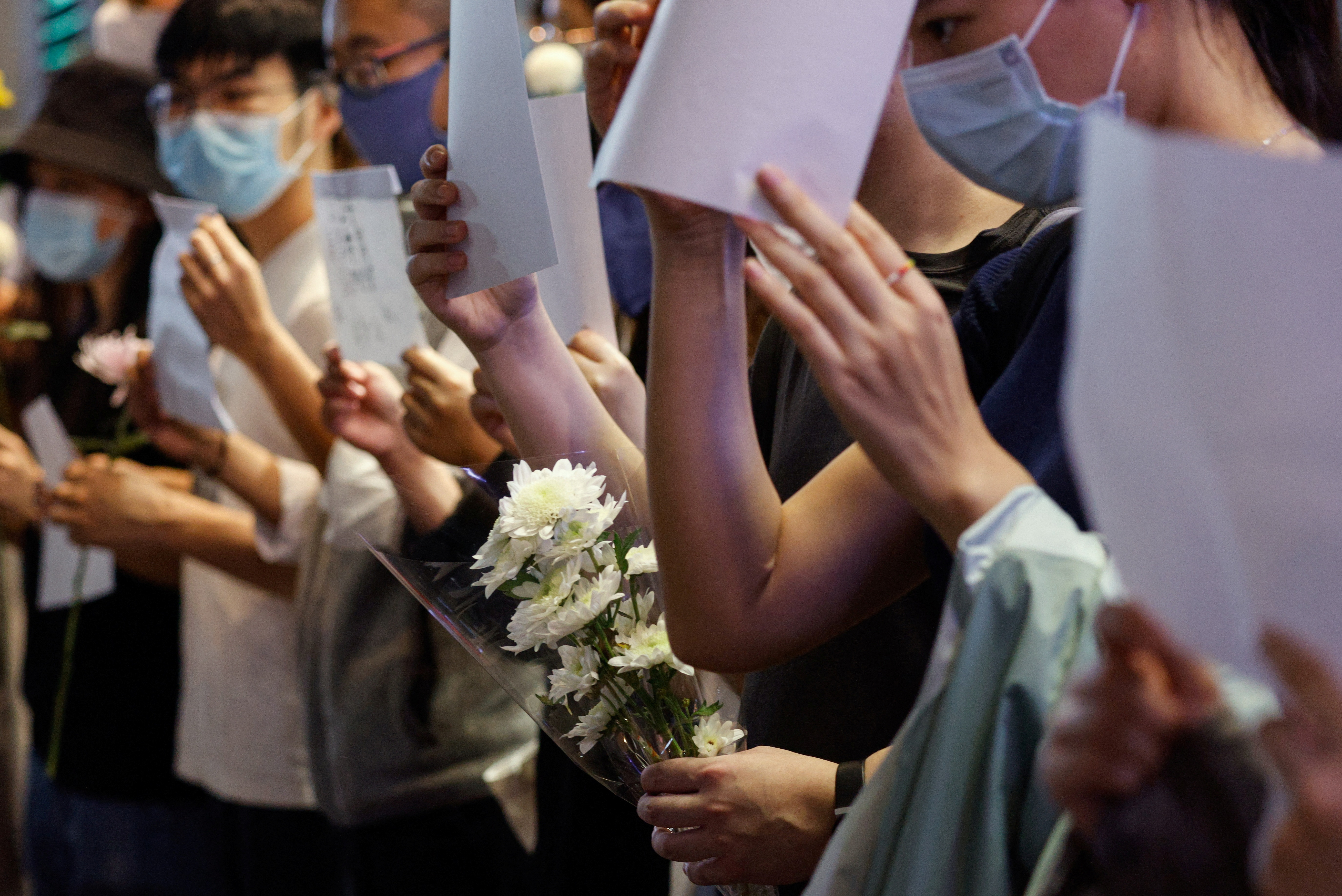Unas personas sostienen hojas de papel blancas y flores en protesta por las restricciones de la enfermedad del coronavirus (COVID-19) en la China continental, durante una conmemoración de las víctimas de un incendio en Urumqi, en Hong Kong, China, el 28 de noviembre de 2022. REUTERS/Tyrone Siu