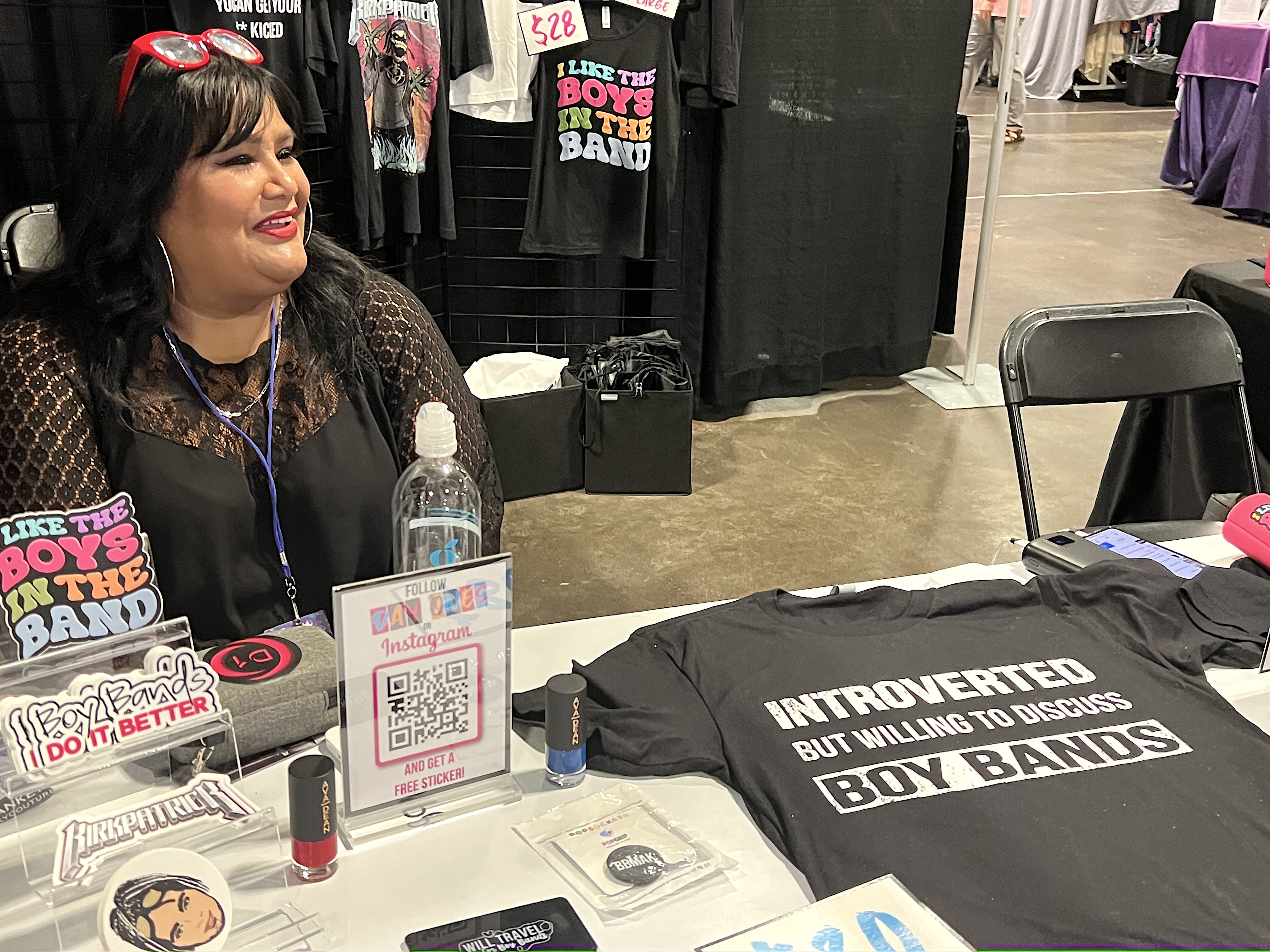 Lisa Sanchez sits at her vendor booth with a t-shirt reading "Introverted but willing to discuss boy bands" at 90s Con at Tampa Convention Center on Sunday, Sept. 17, 2023.
