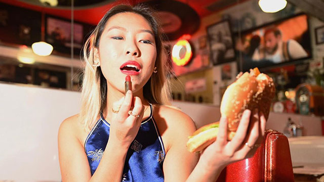 Photo of a woman doing her makeup pretending to use a hamburger as a mirror.