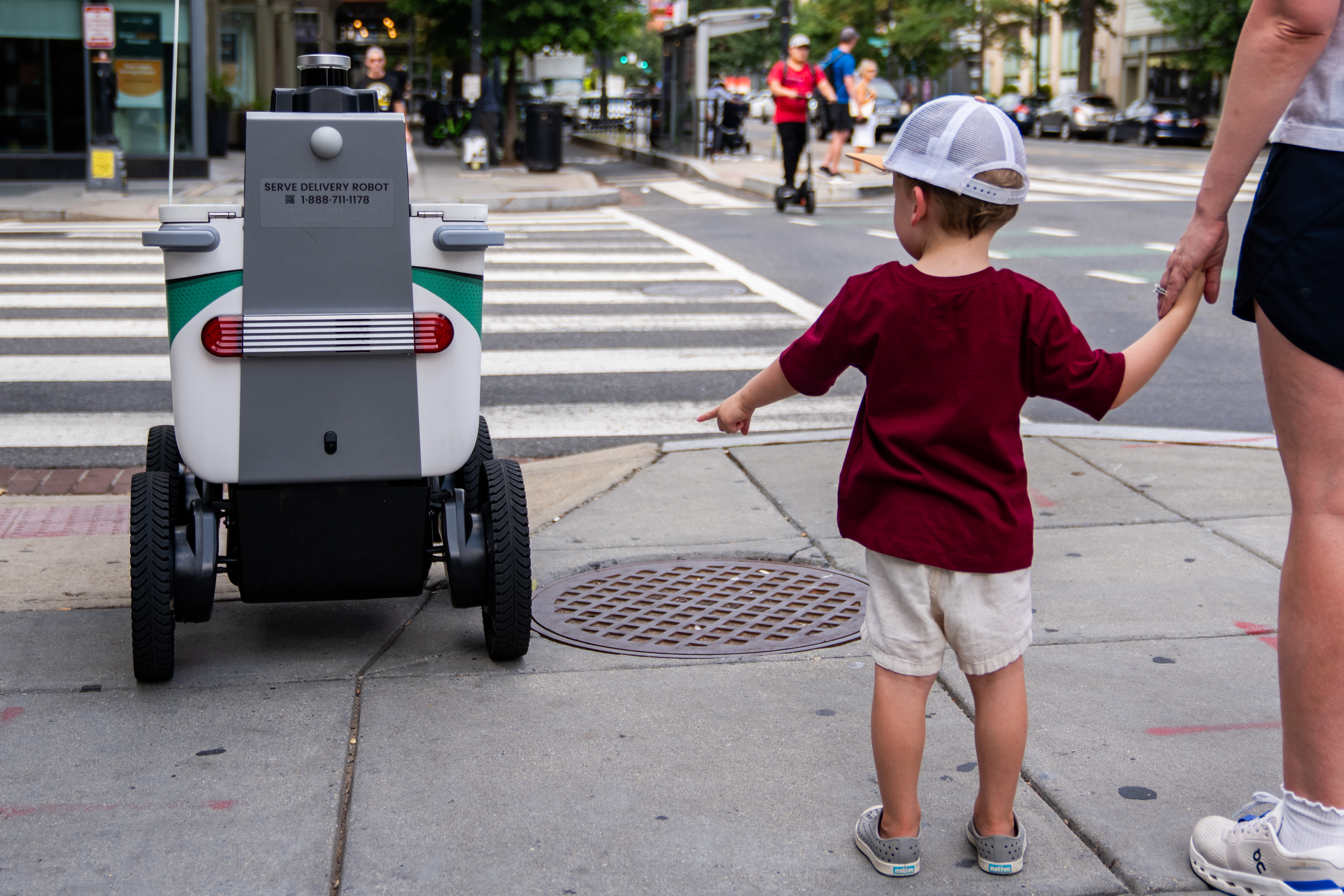 A child points at a food delivery robot. (Allison Robbert/For The Washington Post)