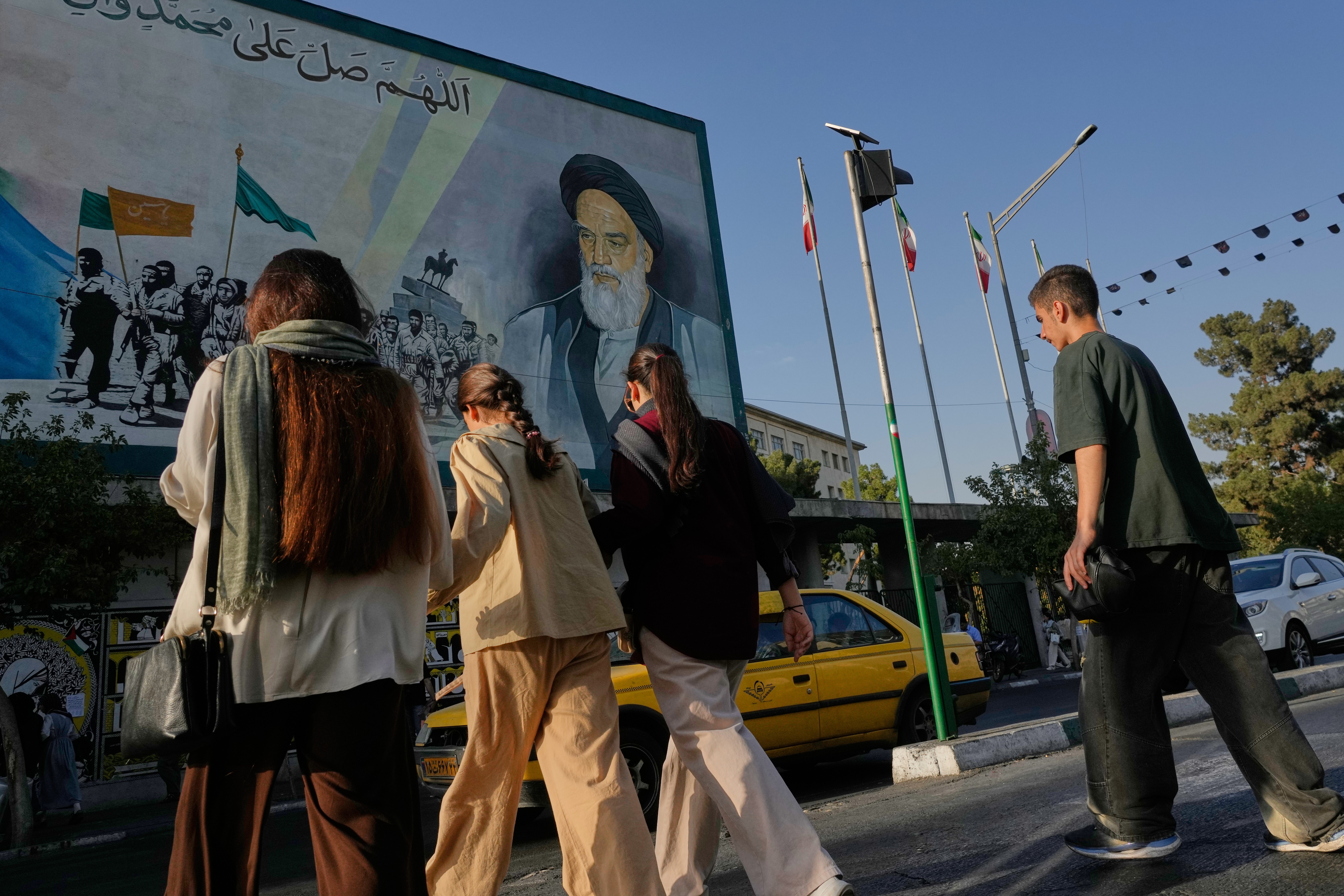 A mural depicting the late Iranian revolutionary founder Ayatollah Ruhollah Khomeini looms over pedestrians in Tehran on Saturday. (Vahid Salemi/AP)