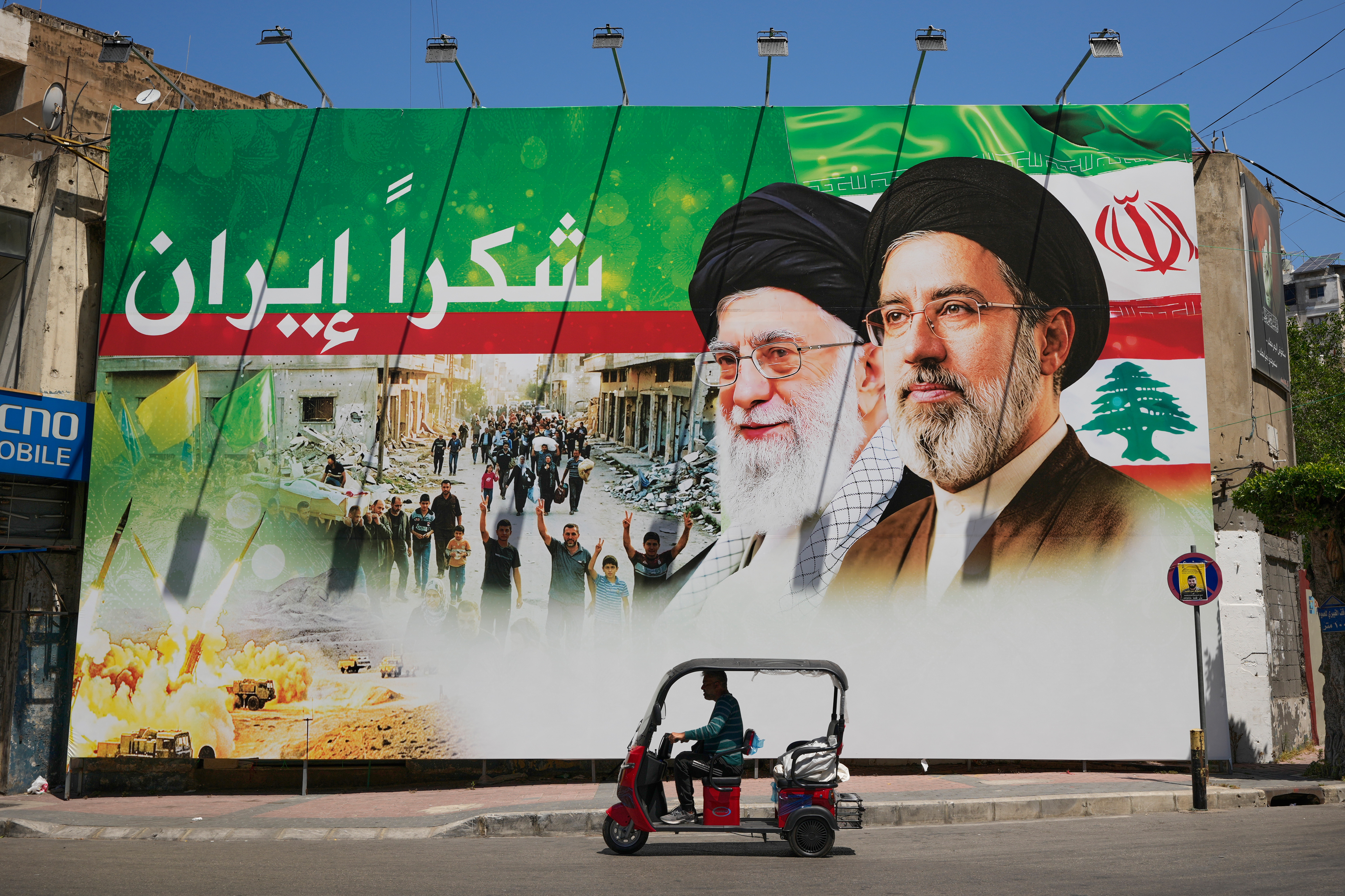 A man rides a scooter past a giant billboard that shows the late Iranian leader Ayatollah Ali Khamenei, center, and Iranian Supreme Leader Ayatollah Mojtaba Khamenei, with Arabic writing that reads: "Thank you Iran," in Dahiyeh, Beirut's southern suburbs, on Monday. (Hussein Malla/AP)