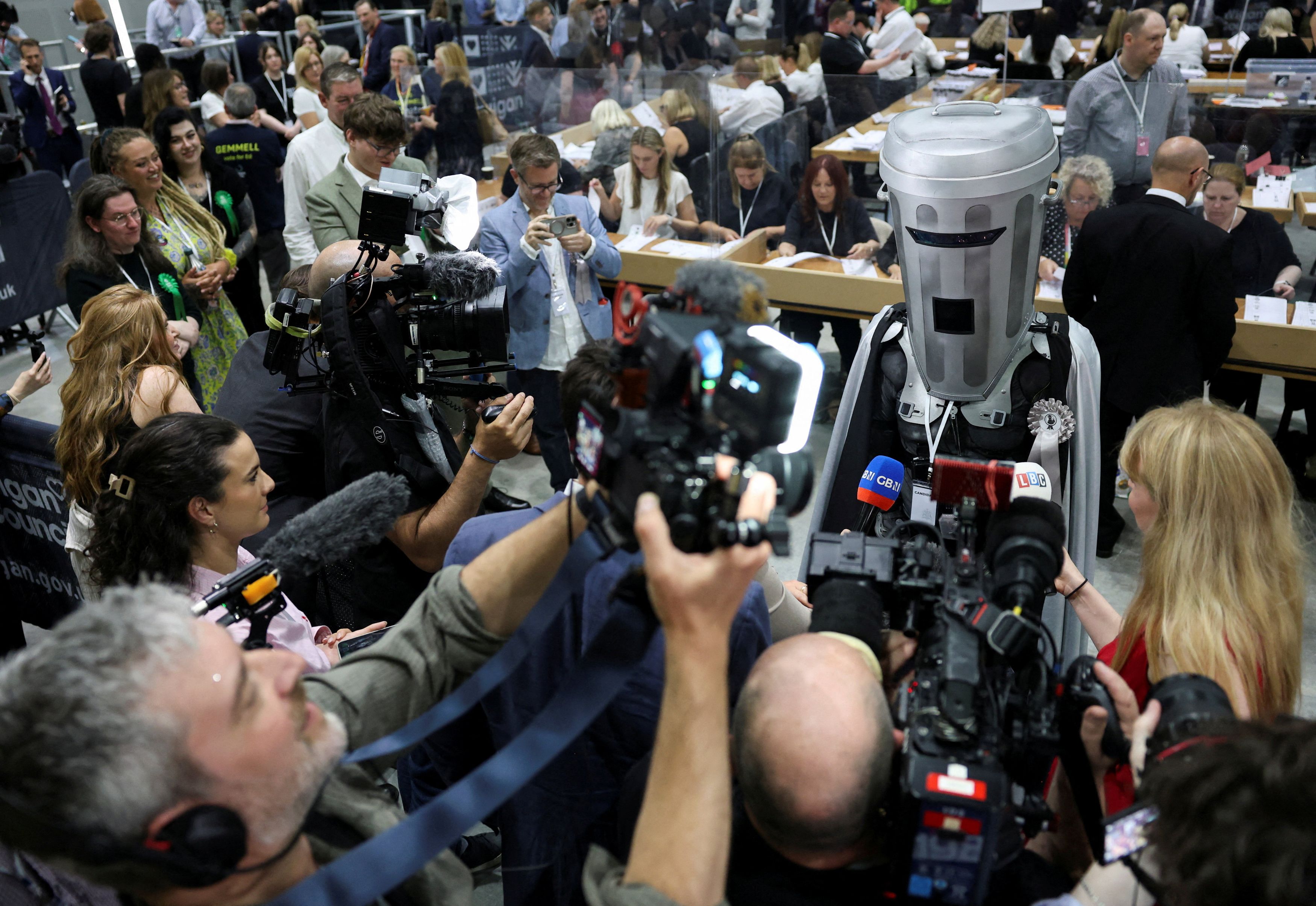 Count Binface speaks to members of the press last month in Wigan, England. The costumed comedy writer is facing Reform UK co-founder Nigel Farage in a parliamentary election. (Temilade Adelaja/Reuters)