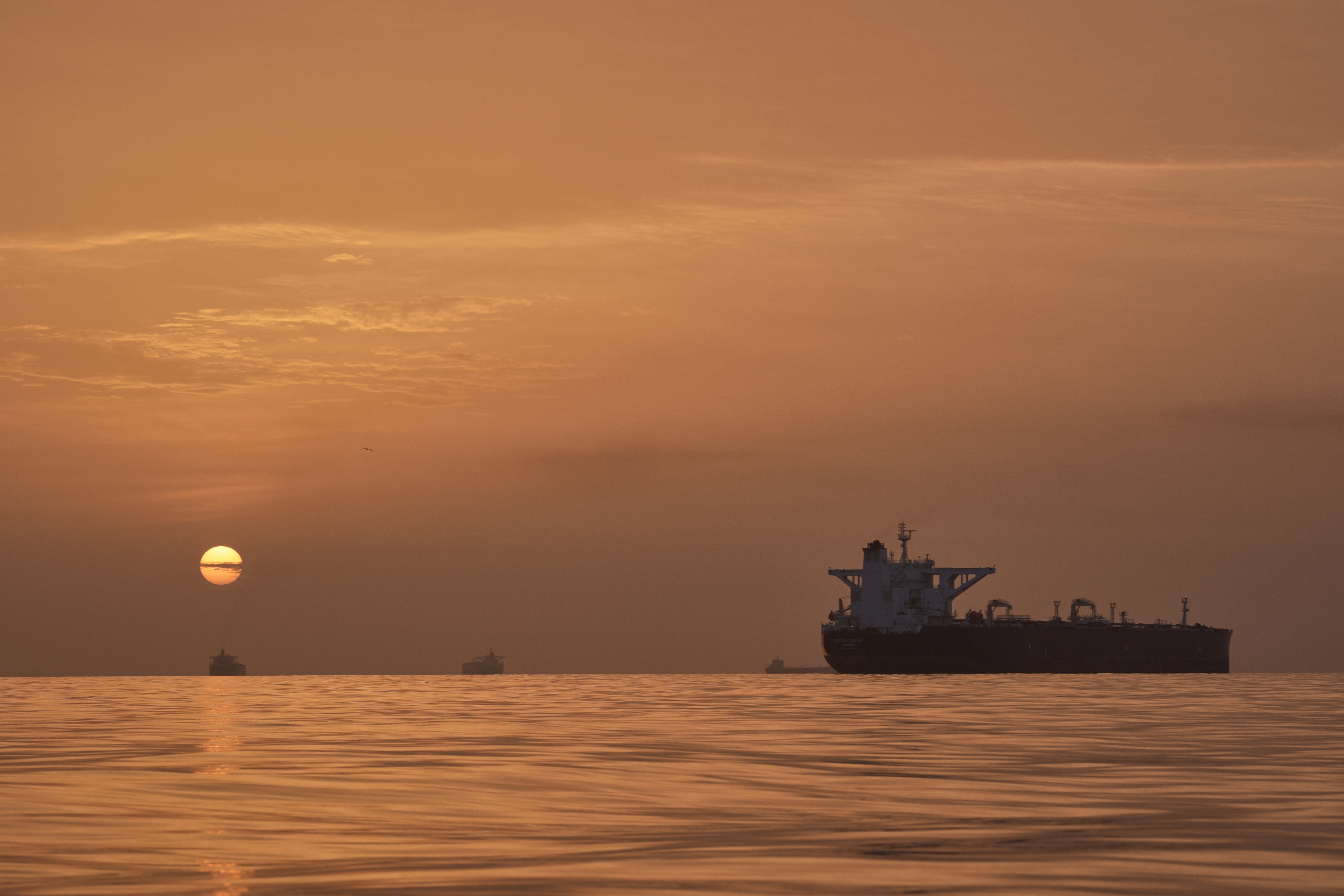 The sun rises behind tankers anchored in the Strait of Hormuz off the coast of Qeshm Island, Iran, on Saturday. (Asghar Besharati/AP)