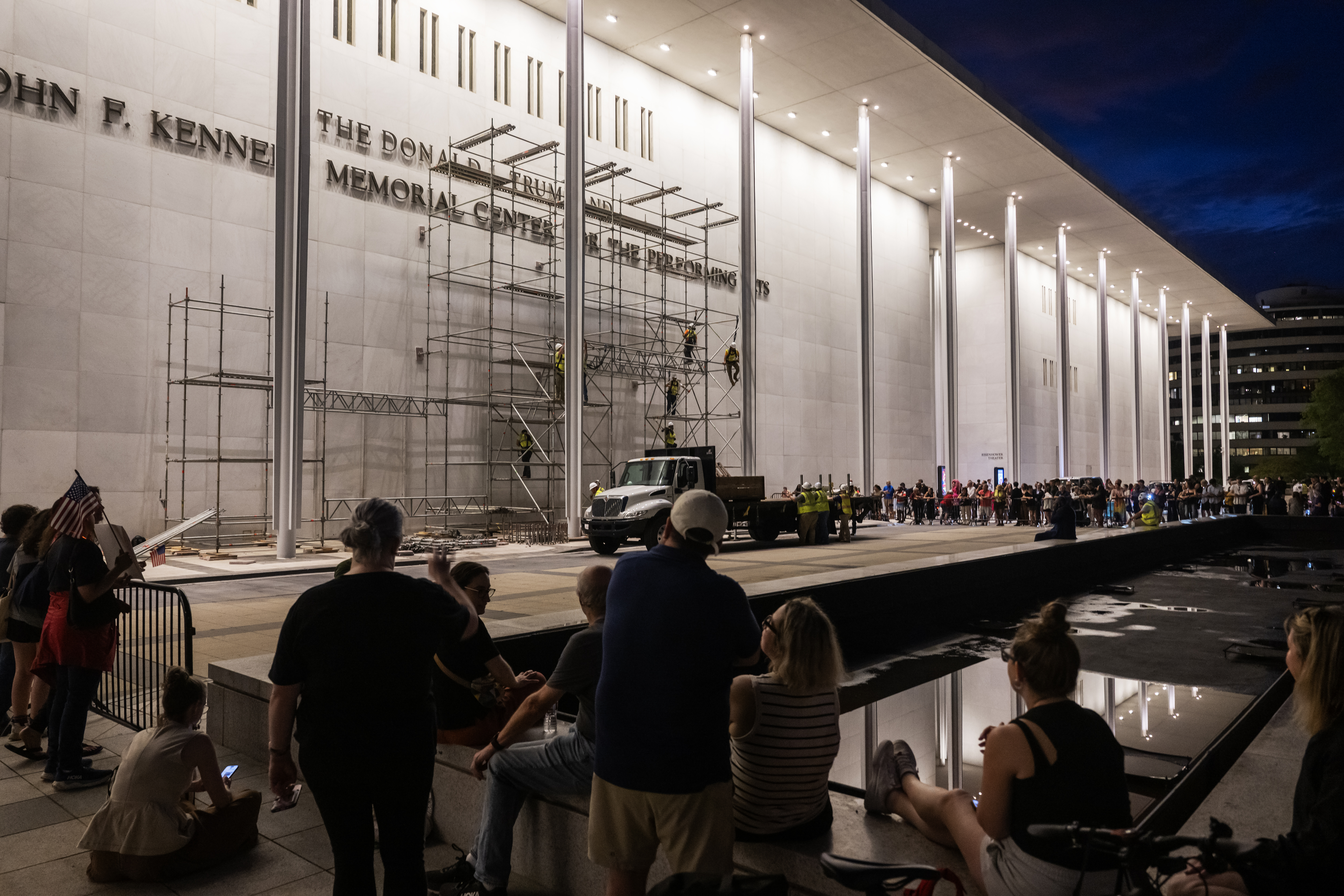 Spectators watch as workers put up scaffolding ahead of a court-mandated deadline to remove President Donald Trump's name from the Kennedy Center's facade. (Craig Hudson/For The Washington Post)