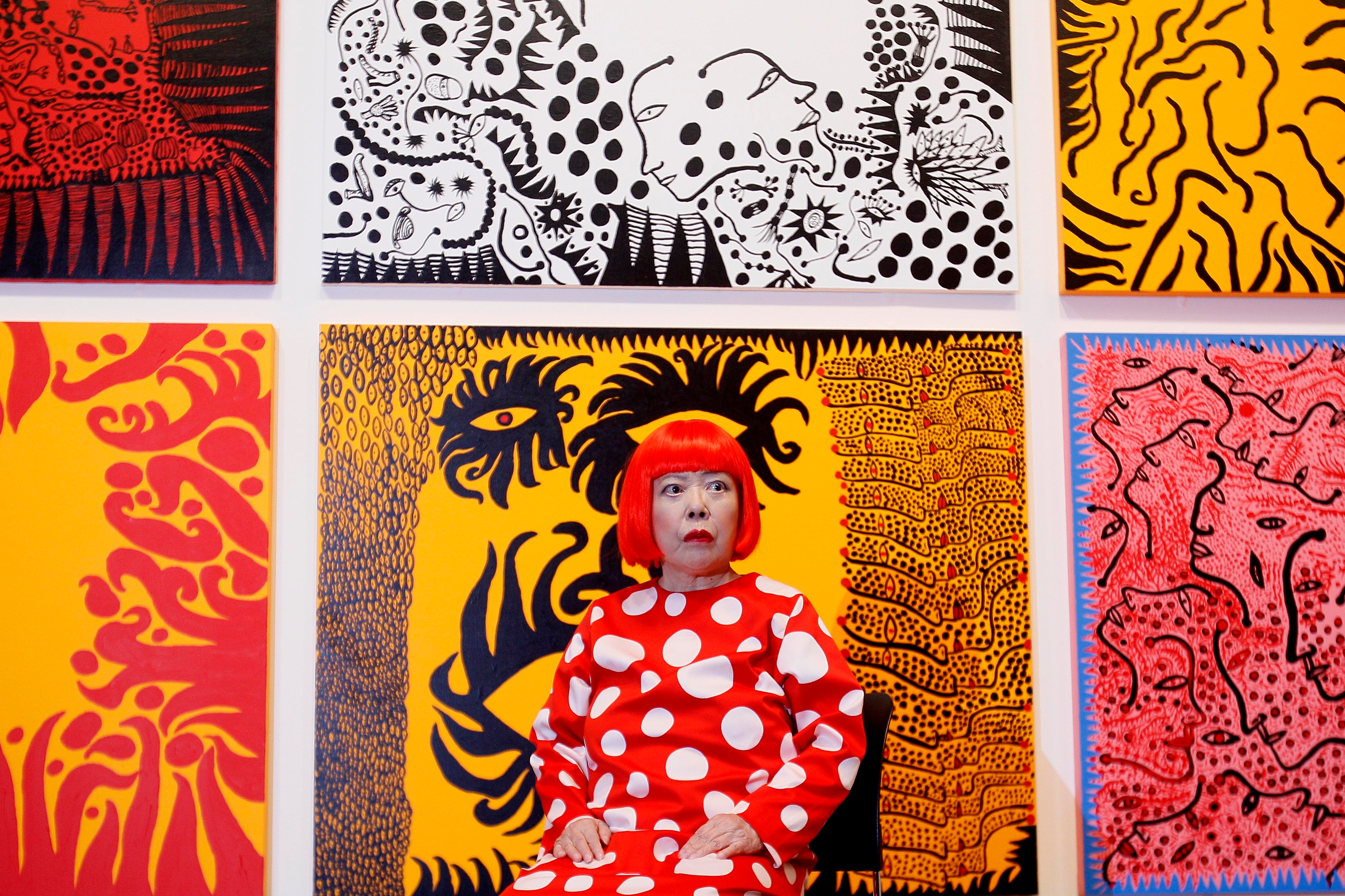 Japanese artist Yayoi Kusama poses in front of her paintings — including "Love Arrives at the Earth Carrying With It a Tale of the Cosmos," bottom row, center — on display at the Tate Modern in London in 2012. (Kirsty Wigglesworth/AP)