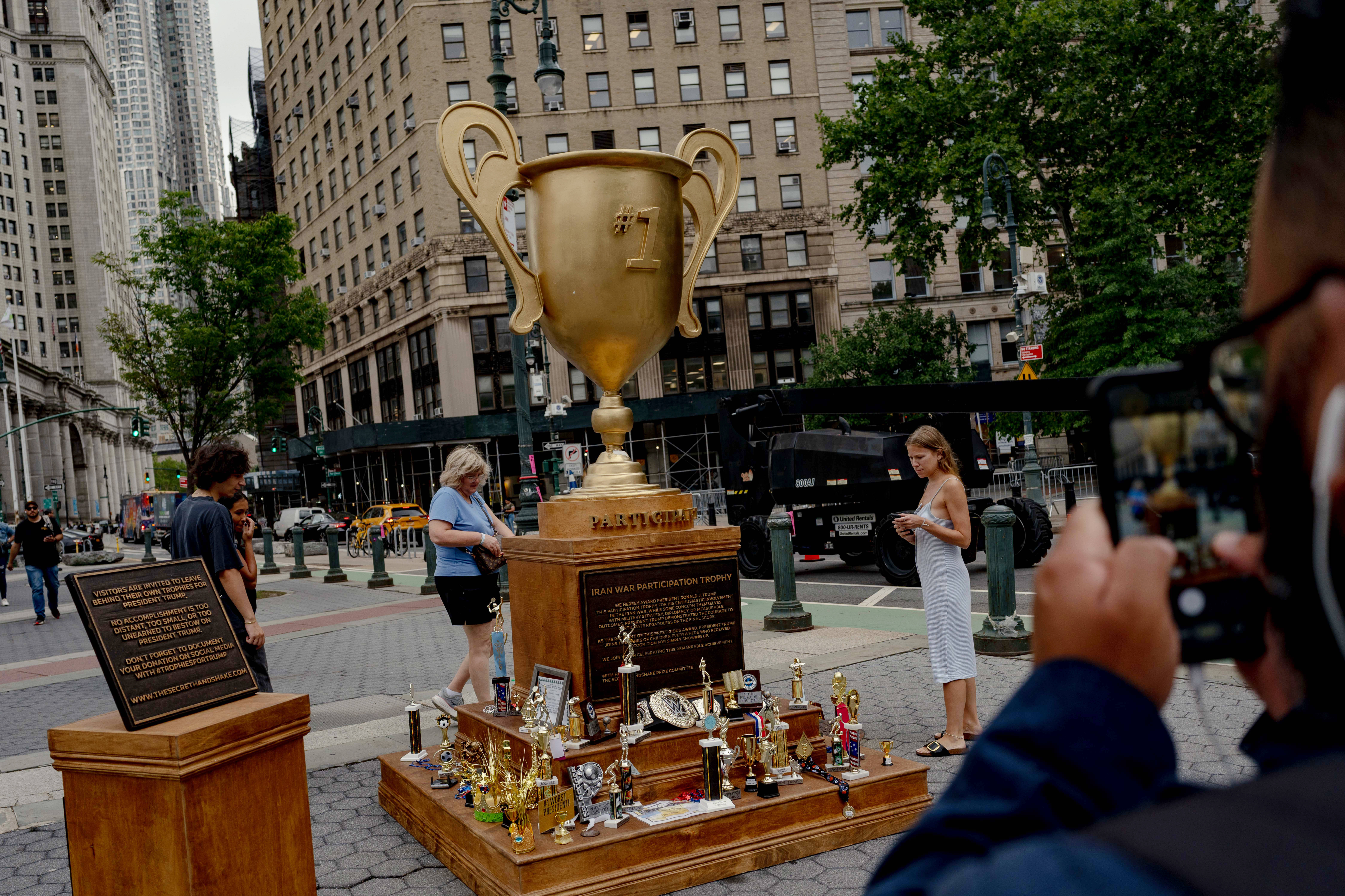 Passersby examine the Secret Handshake's “Iran War Participation Trophy” installation on Wednesday in New York's Foley Square. (Amir Hamja/For The Washington Post )