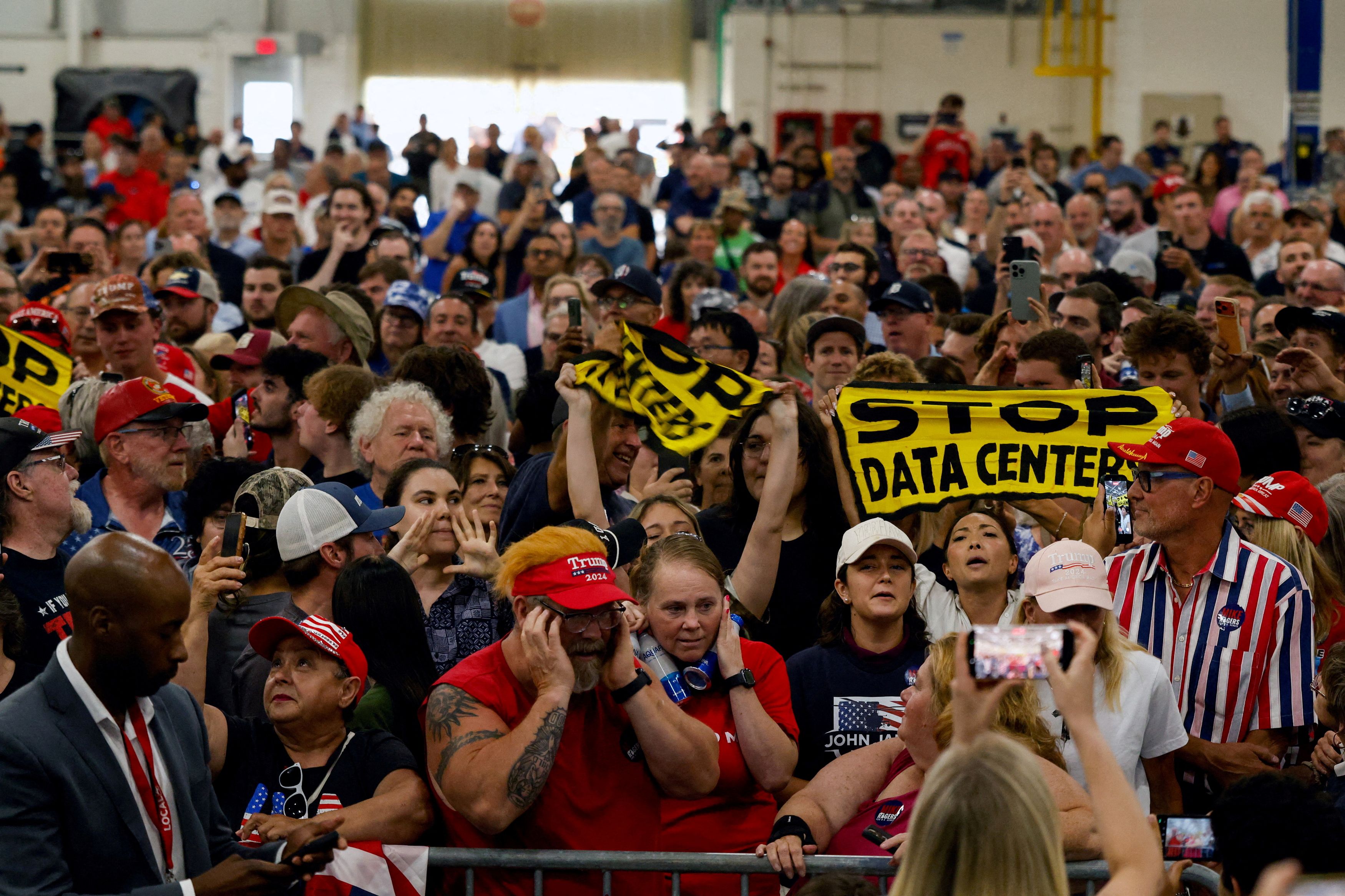 People hold up signs protesting the building of data centers on the same day President Donald Trump gave a speech at the General Motors Proving Ground in Milford, Michigan. (Carlos Osorio/Reuters)