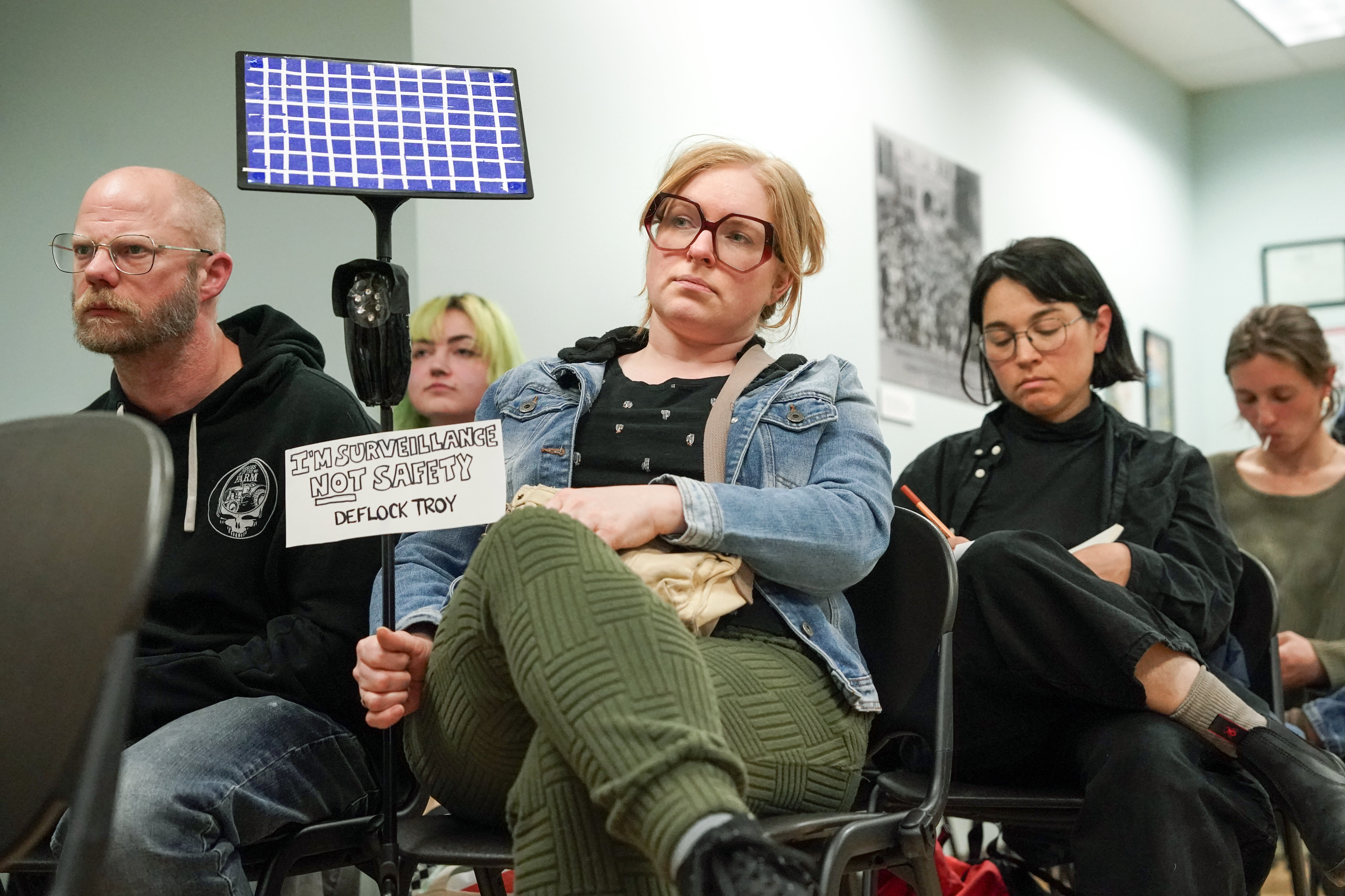 Bri Harrington holds a sign and a handmade Flock camera prop during a council meeting in Troy, New York, in April. (Cindy Schultz/For The Washington Post)