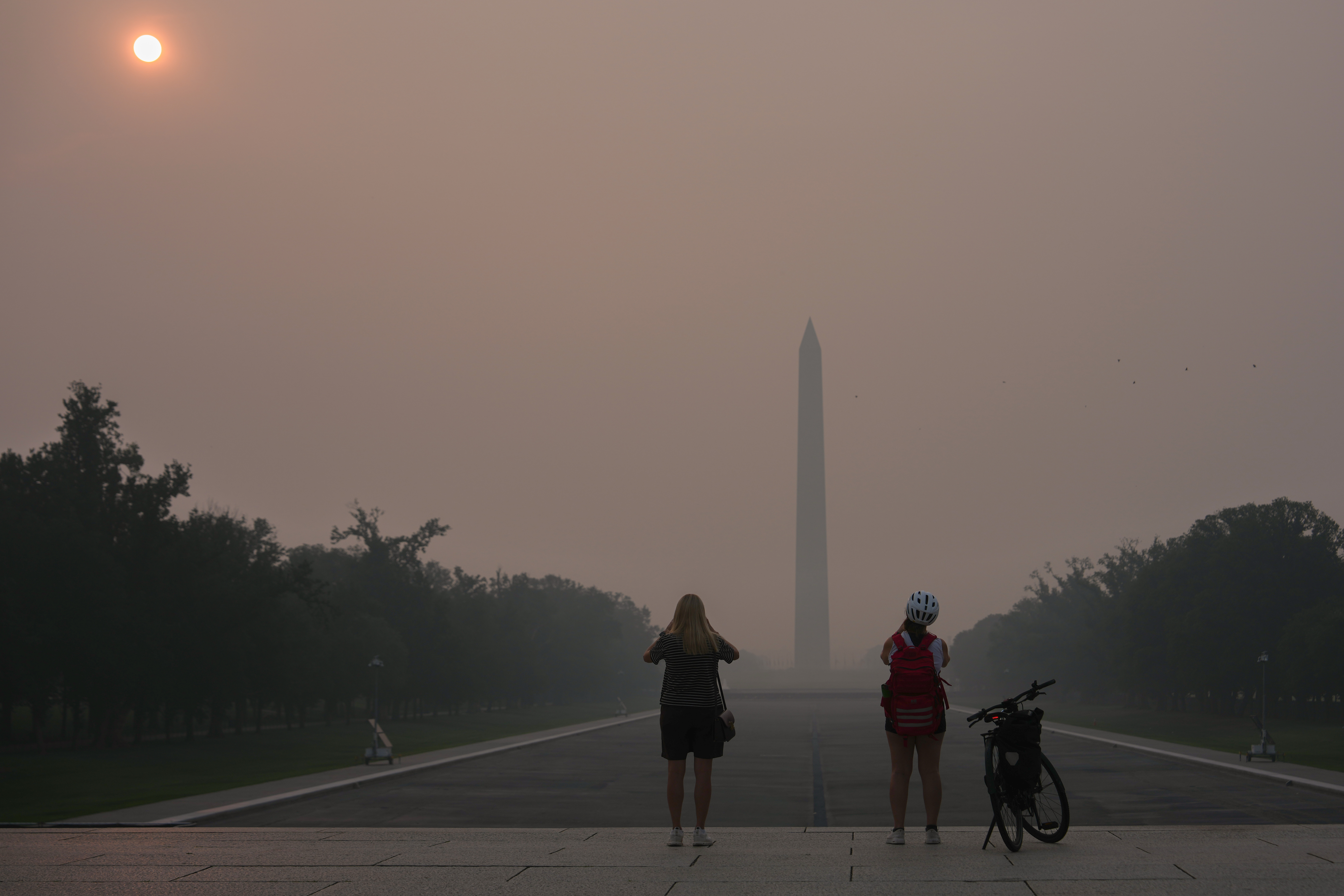 Wildfire smoke obscures the sun as people stop to photograph the Washington Monument and Reflecting Pool in D.C. on Friday. (Julia Demaree Nikhinson/AP)