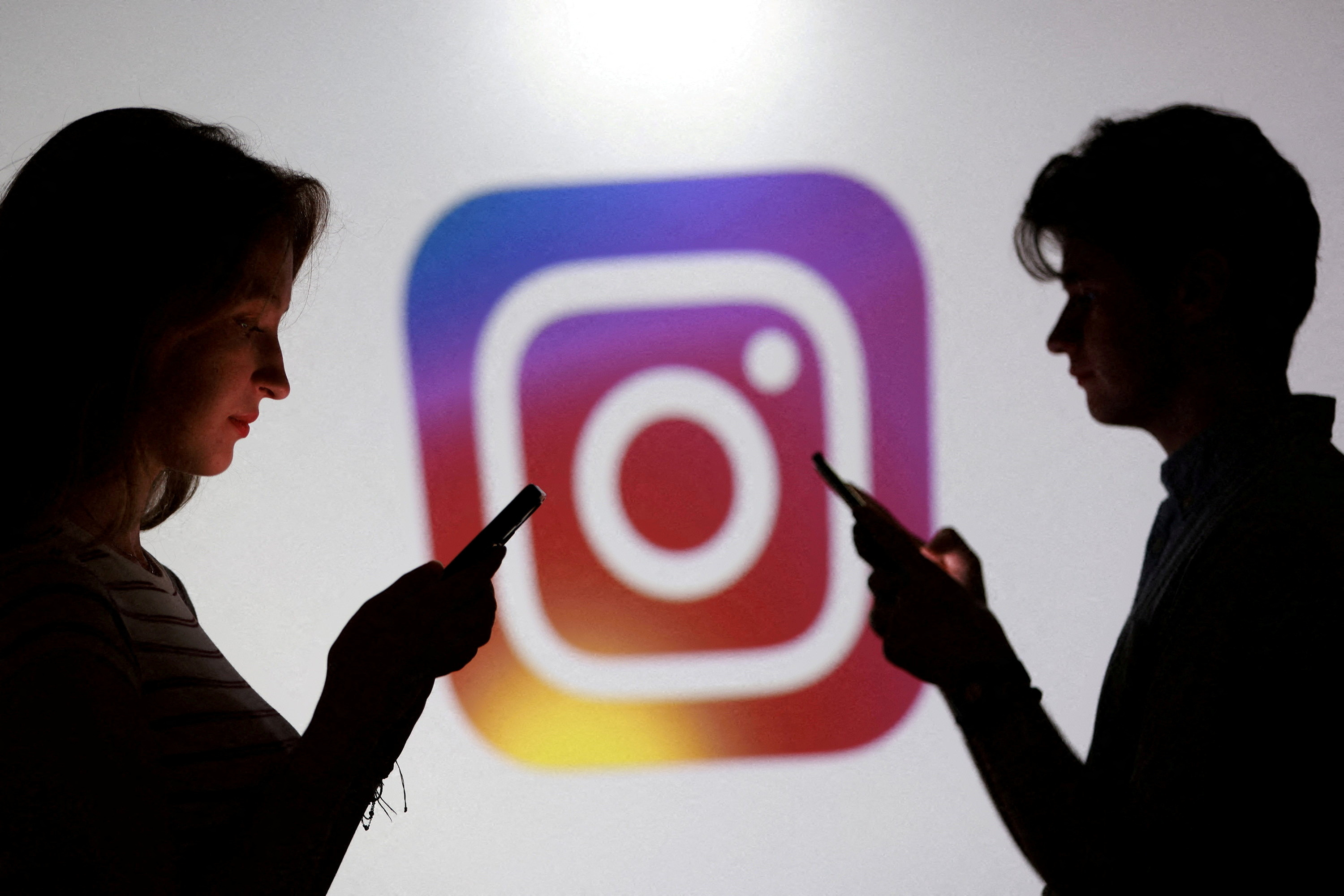 Teens check their smartphones in front of an Instagram logo. (Dado Ruvic/Reuters)