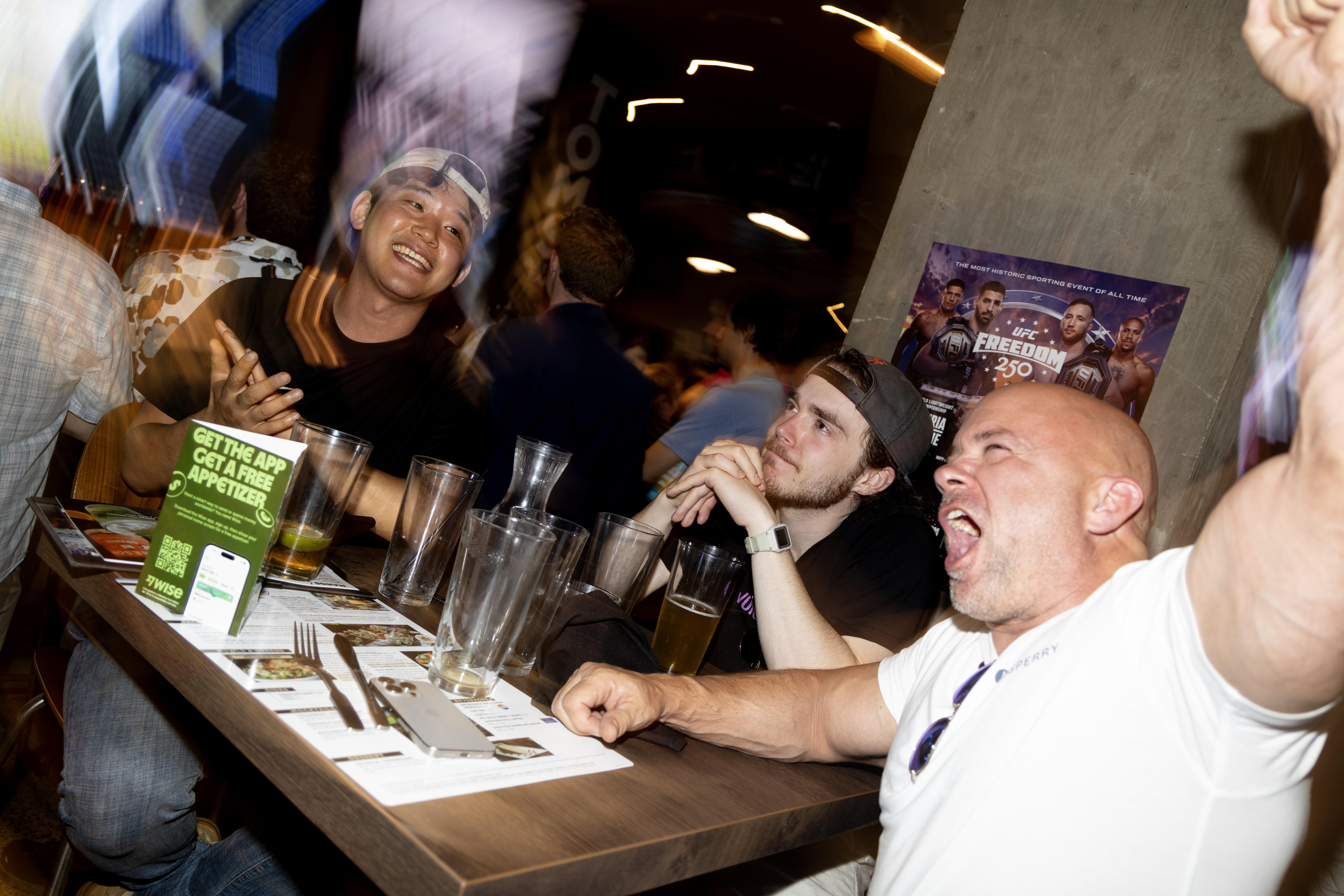 Youngrak Seong and the son-father duo of Isaac and Chuck Martin, react to the second match at UFC Freedom 250 in Tom’s Watch Bar. (Christine Kao/The Washington Post)