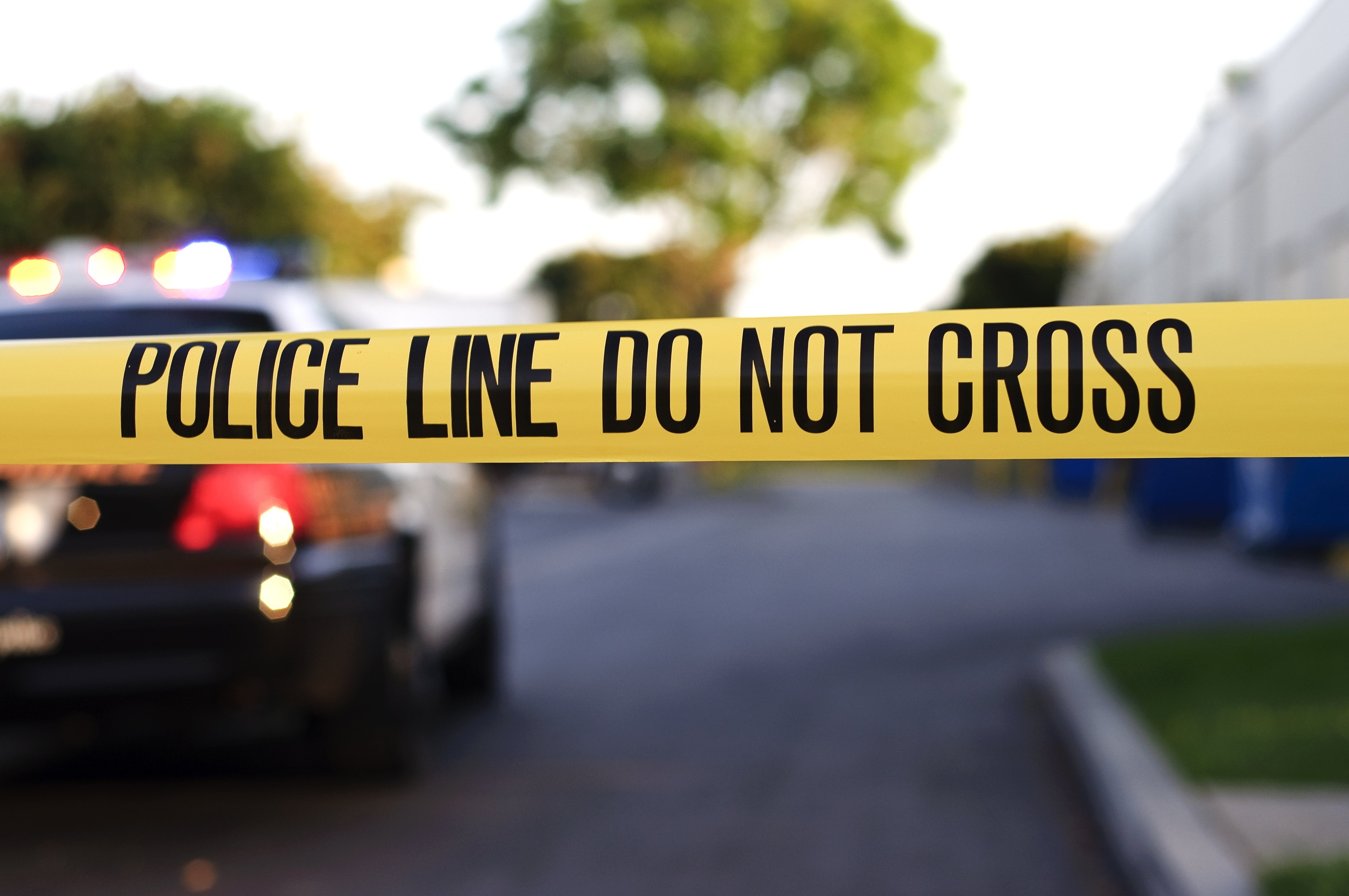 A blurred police car in the background behind yellow crime scene tape. (iStock)